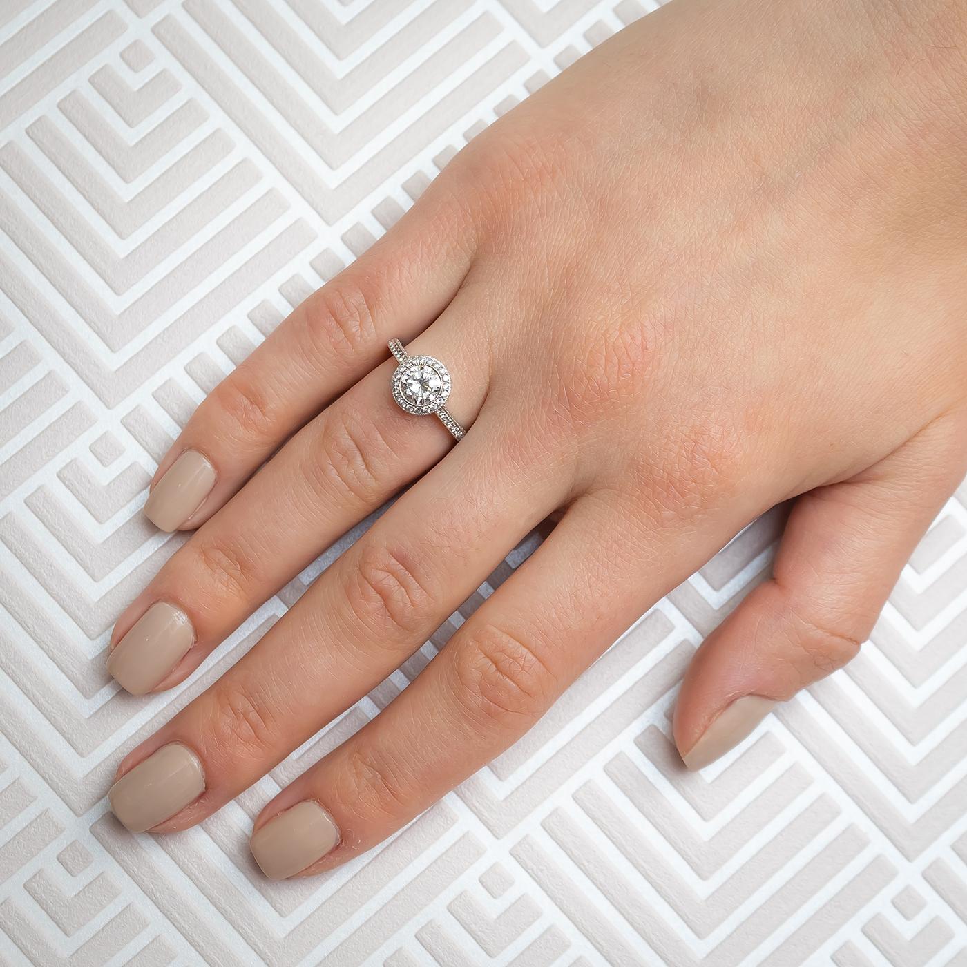 A modern solitaire diamond halo design ring, set with a 0.85ct round brilliant-cut diamond, in our opinion the colour is J to K and our opinion of the clarity is I1, with surrounding micro pavé set round brilliant-cut diamonds, forming a halo around