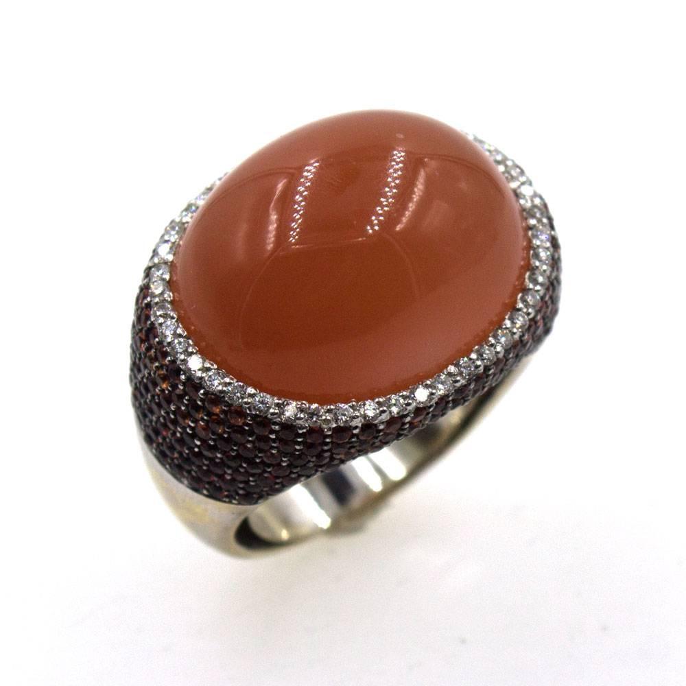 This fabulous modern statement ring features a large cabochon chalcedony gemstone (17 x 20mm) surrounded by a row of white round brilliant cut diamonds. There are approximately .30 carat total weight of diamonds. In addition,  orange sapphires add