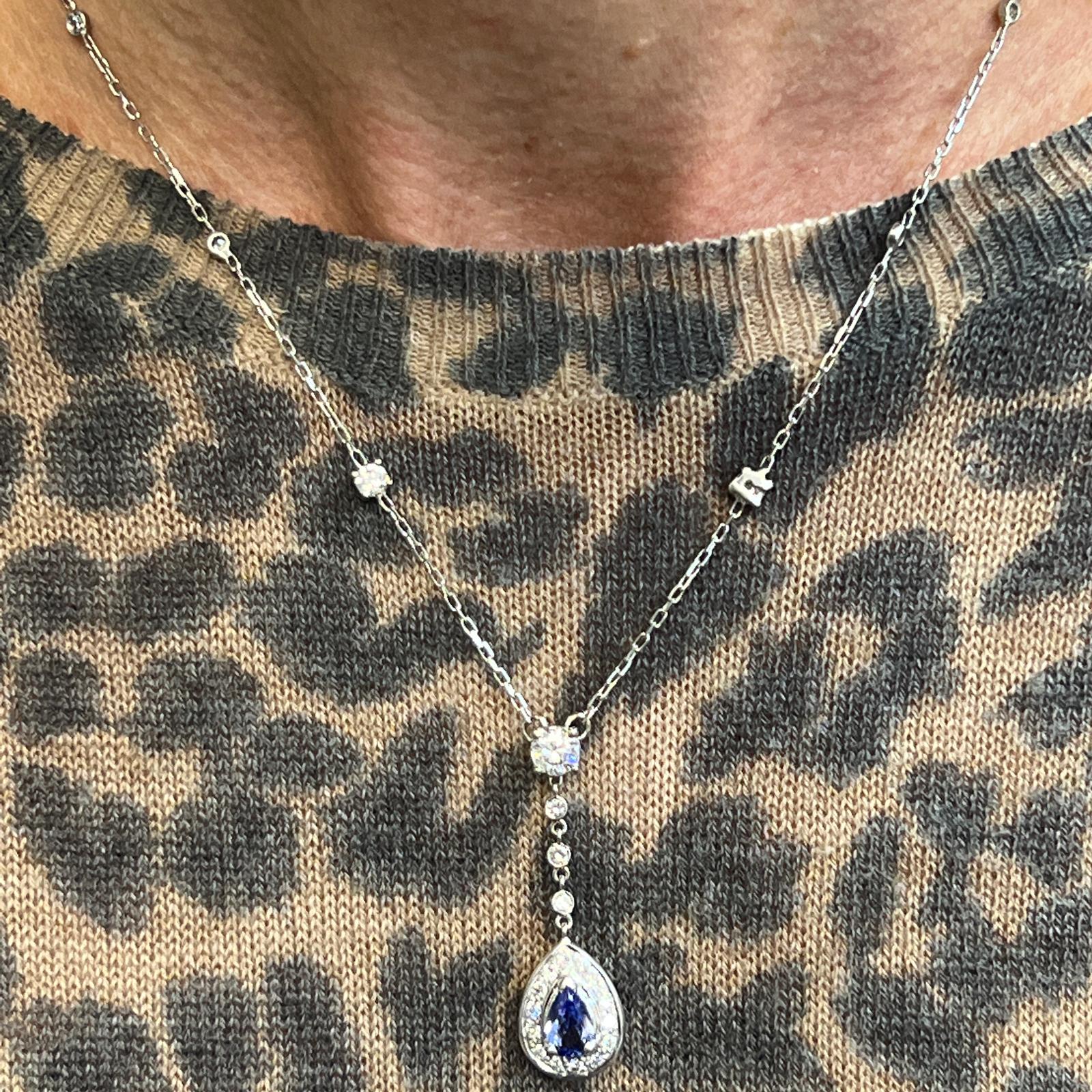 Diamond and tanzanite drop necklace fashioned in 14 karat white gold. The necklace drop features an .81 carat pear shape tanzanite gemstone surrounded by a halo of round brilliant cut diamonds. A 1/2 carat round brilliant diamond is set at the