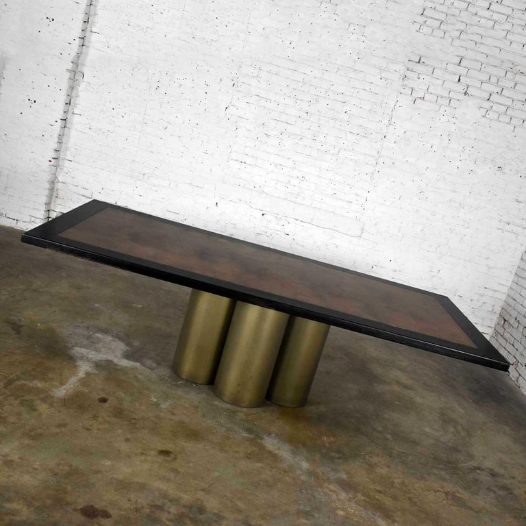 Fantastic modern dining table with a four-cylinder metal pedestal base, dyed black oak tabletop frame, and aged brass center insert in the style of Pace. Gorgeous, refinished condition with beautifully aged and distressed patina on the wood top and
