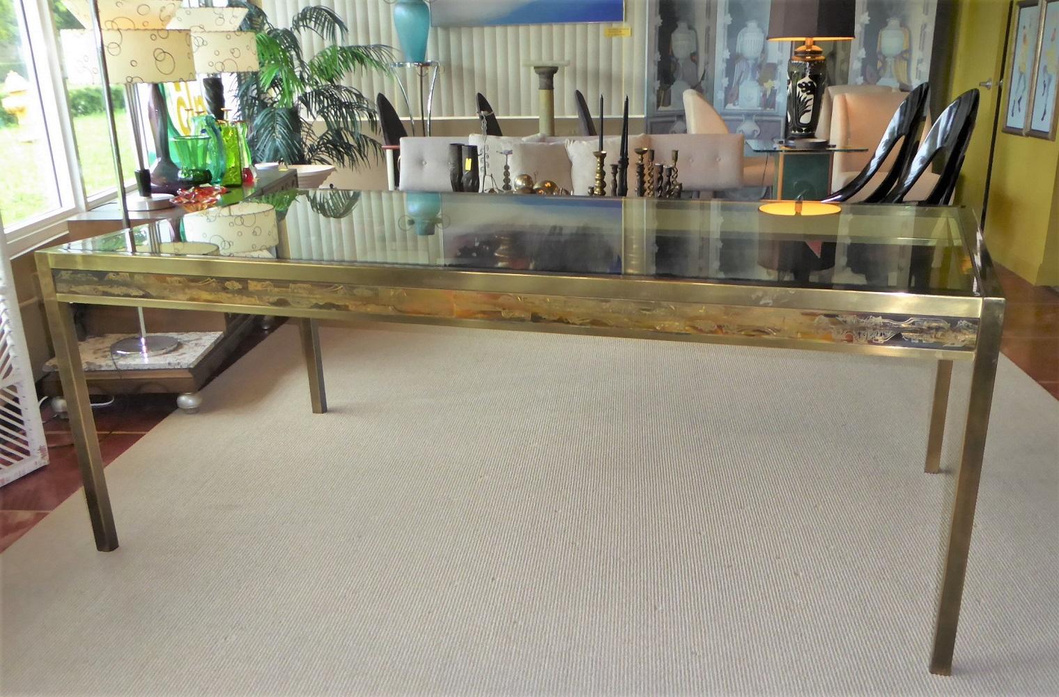 Large Mastercraft brass and glass dining table with panels designed by Bernhard Rohne. Antique brass frame with acid etched decorated panels on its apron and an inset thick beveled glass top. The brass is beautifully patinated although it has some