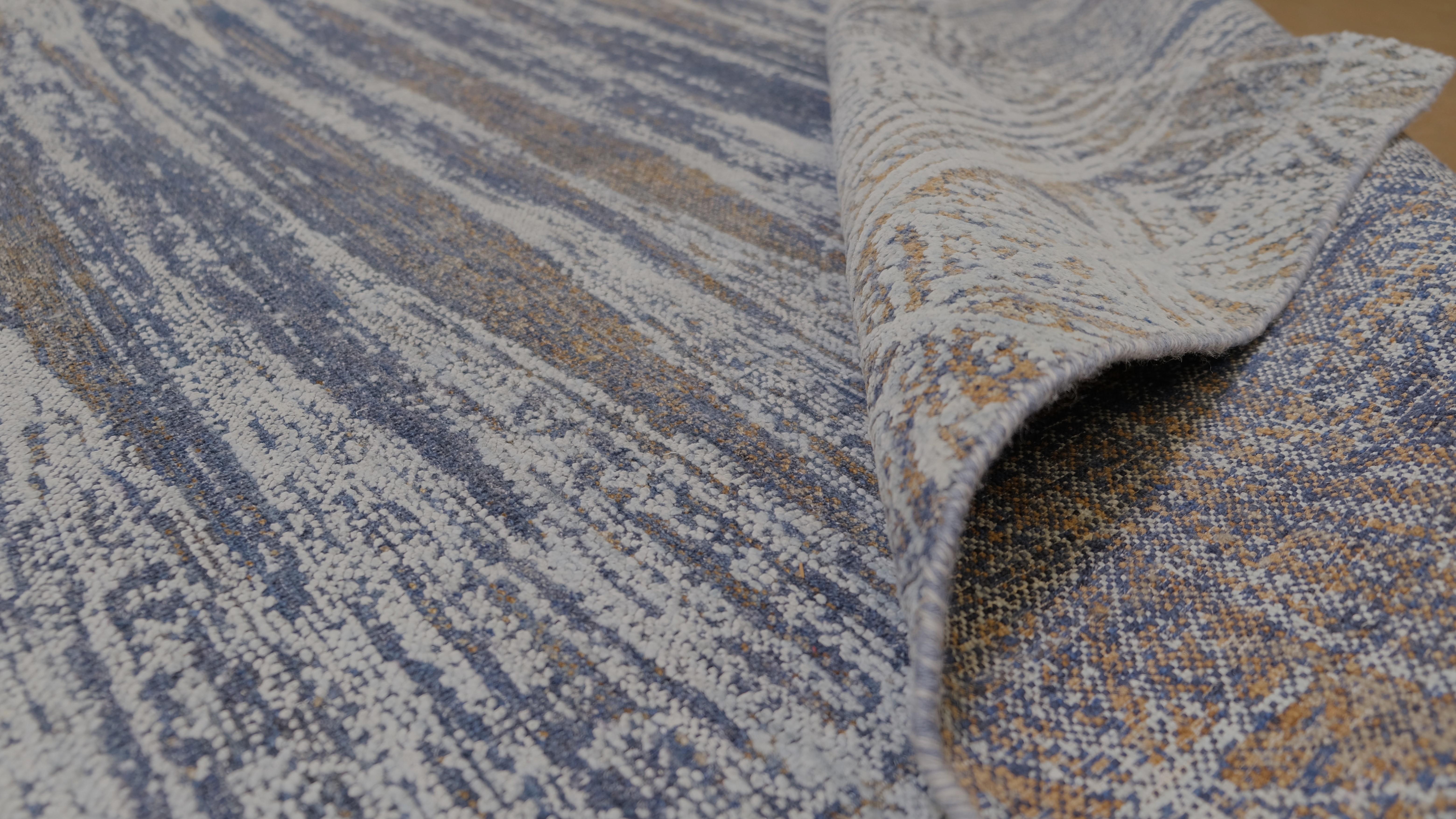 Introduce la elegancia atemporal en tu hogar con esta alfombra de lana y seda anudada a mano, meticulosamente elaborada por hábiles artesanos. Esta impresionante alfombra presenta un diseño desgastado en tonos azul, marrón dorado y beige, creando