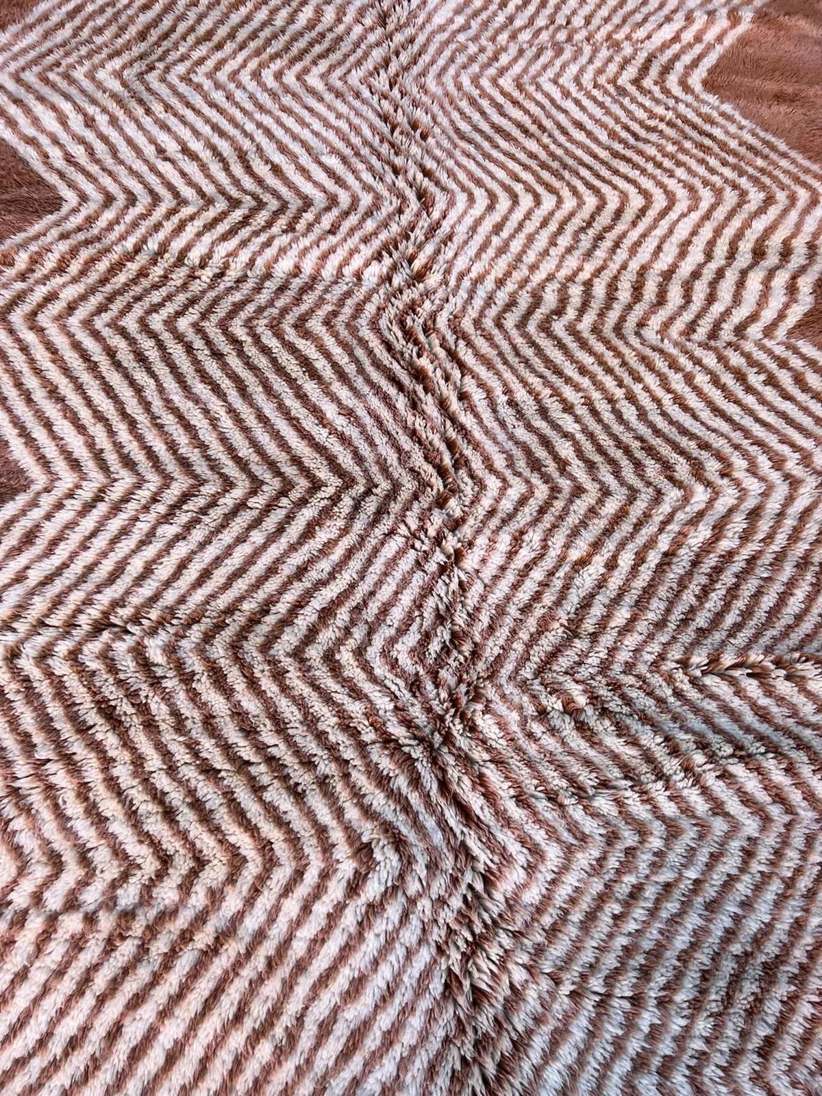 This neutral handwoven Moroccan rug was made by hand by skilled artisans in the Atlas Mountains using the highest quality M'Rirt wool. A pleasing geometric line design sits on neutral, dusty rose wool base. This rug measures about 5.8 x 9.3 feet and
