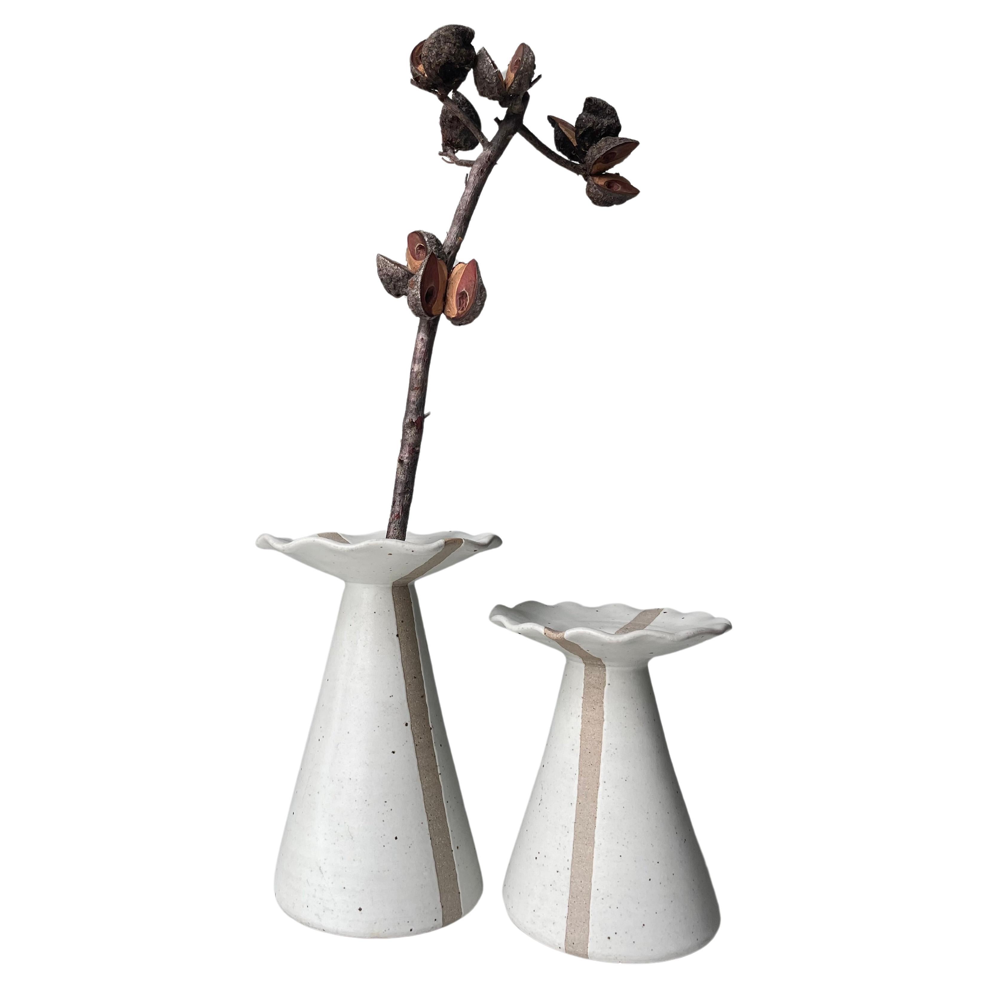 Handmade set of two vases / candlesticks in smooth ceramic material. Modern matte chalk grayish white glaze with small brown dots and a light brown broad unglazed line placed symmetrically from the base to the top and across the wide frilled top and