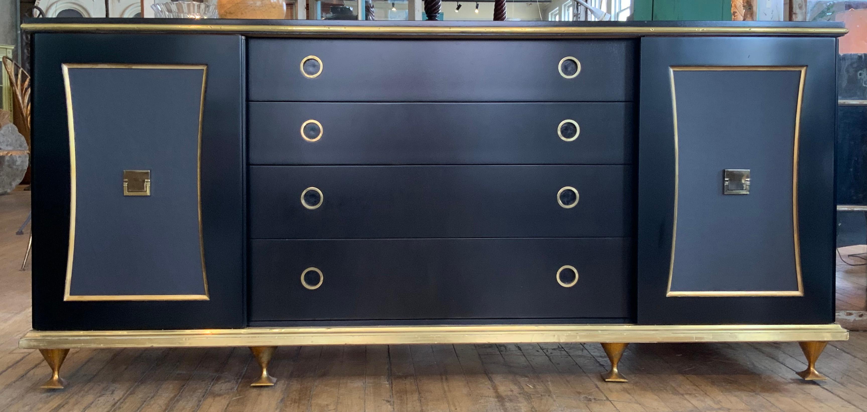 An incredible 1950s modern cabinet designed by Renzo Rutili for Johnson Furniture. Raised on charming brass feet and a brass base, the case has been ebonized and the doors are paneled in gray/blue leather. The center doors slide apart to reveal a