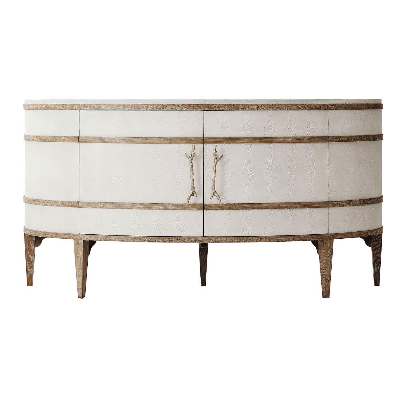 Modern embossed leather panelled demi lune sideboard cabinet with figured Ofram veneers and solid Oak moldings in a cerused finish. The two door cabinet with champagne finished textured coral cast brass handles and the interior having adjustable