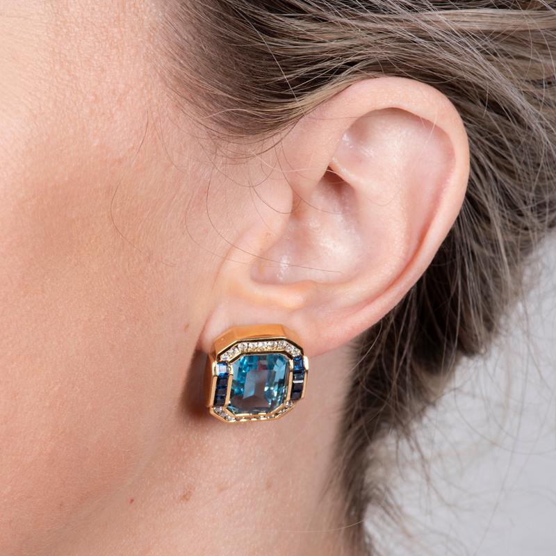 Ces boucles d'oreilles modernes présentent des lignes épurées avec des pierres de topaze bleue en forme d'émeraude, accentuées par des diamants ronds d'un poids total de 0,80 carat et des baguettes de saphir d'un poids total de 1,80 carat. Ils sont