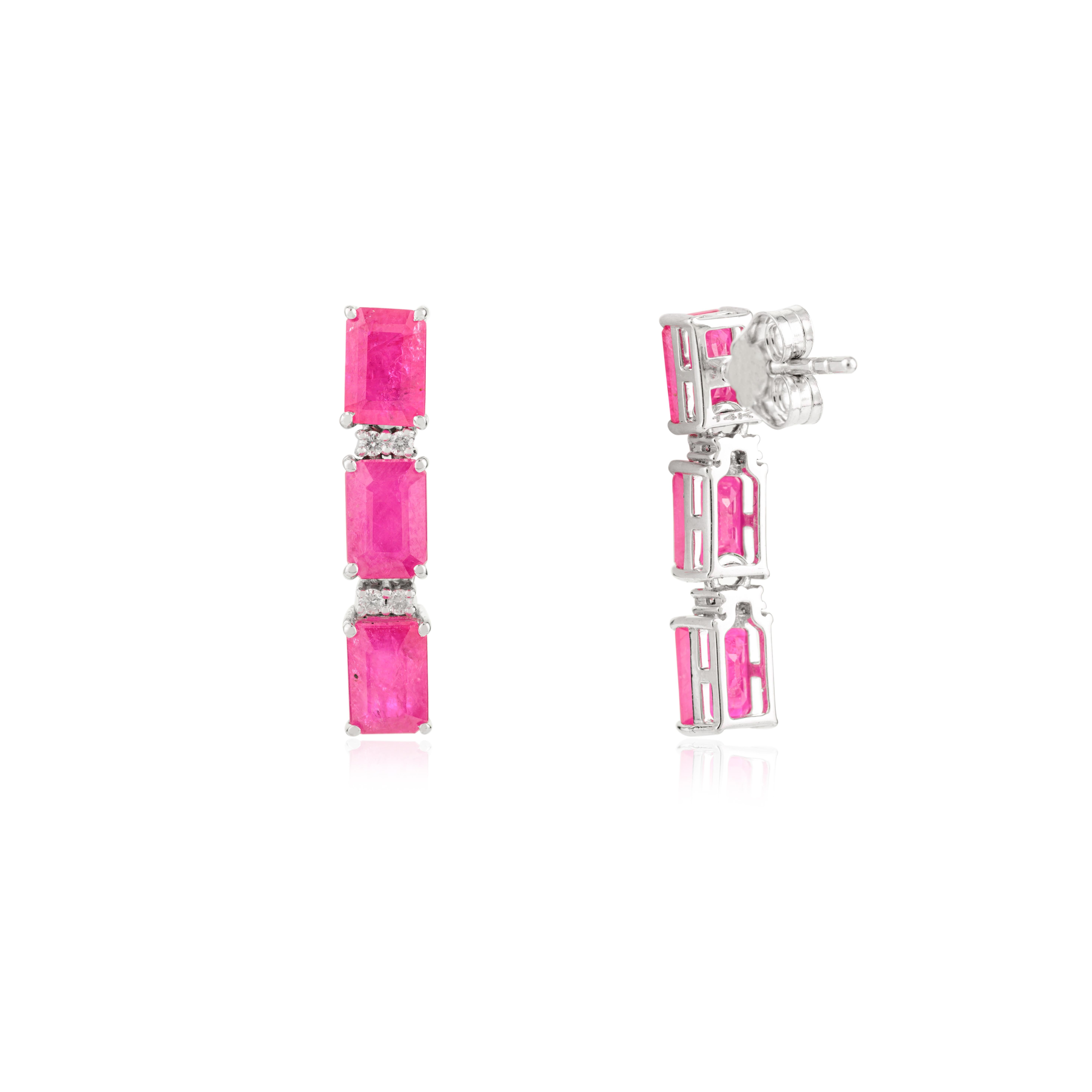 Bold yet refined, this striking pair of earrings is crafted in 14k white gold and showcases a total of 4.62 carats of vivid emerald-cut pink ruby gemstones. Arranged in an elegant vertical drop design, each stone is separated by shimmering diamond