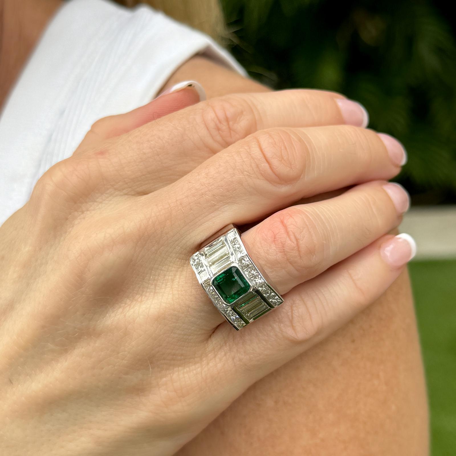 Beautiful bezel set emerald and diamond band crafted in 18 karat white gold. The approximately 1.71 carat natural green emerald is bezel set with surrounding baguette and princess cut diamonds weighing approximately 3.36 carat total weight. The