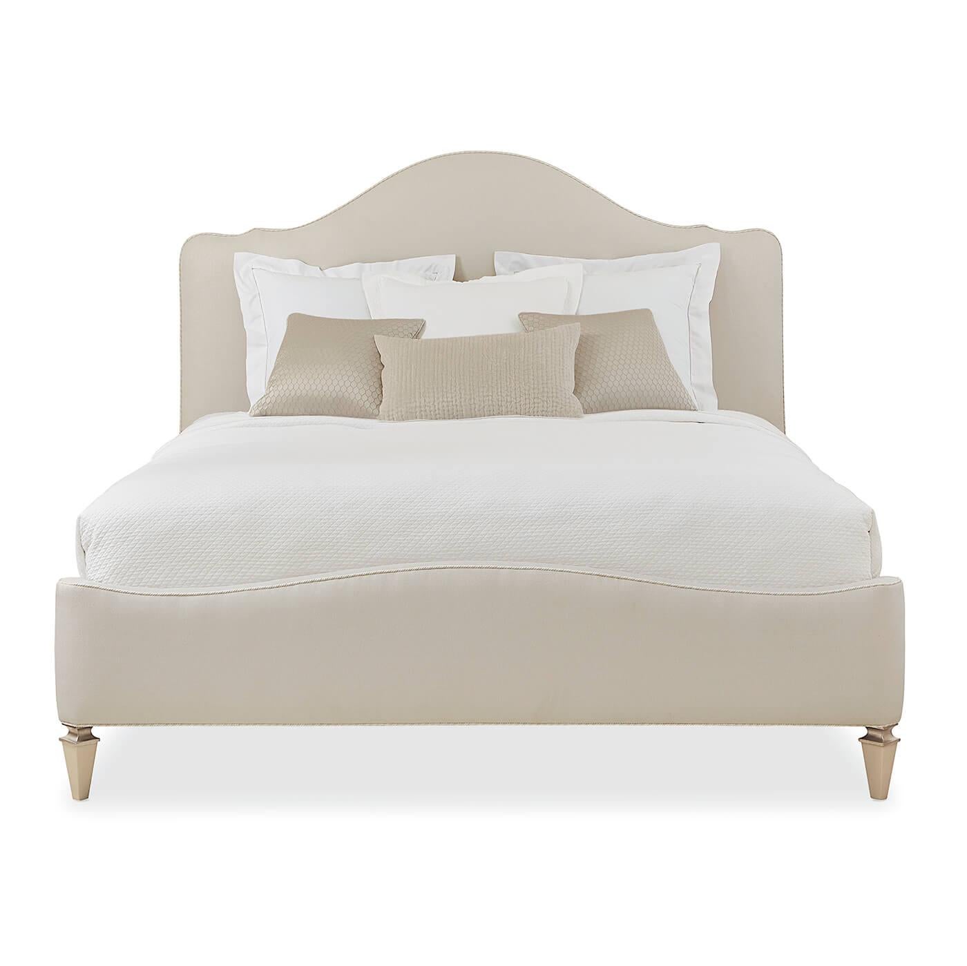 Un lit king anglais moderne à dos de chameau avec des pieds coniques carrés en bois apparent dans des tons riches de Sparkling Argent. La tête et le pied de lit de ce lit glamour sont recouverts d'un tissu luxueux et agrémentés de cordons