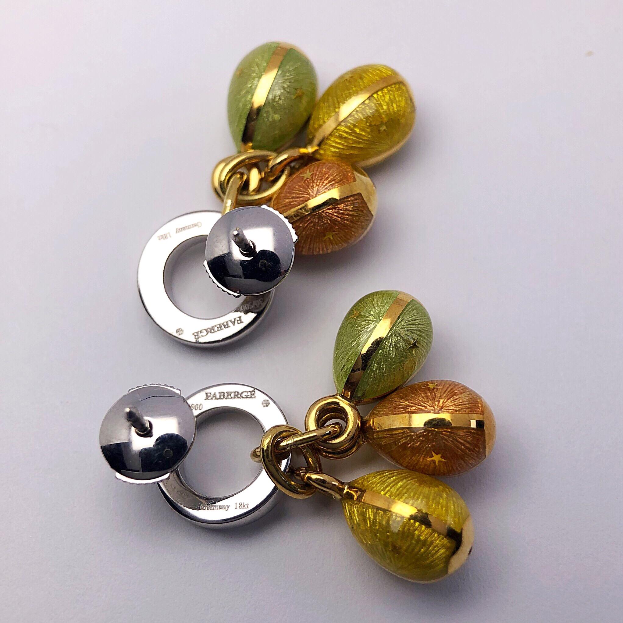 These modern 18 karat yellow gold Faberge earrings by Victor Mayer feature 3 hanging eggs in peach, yellow and mint  guilloche enamel. The eggs are hanging from an 18karat white gold and diamond open circle. The earrings have a white gold post back.