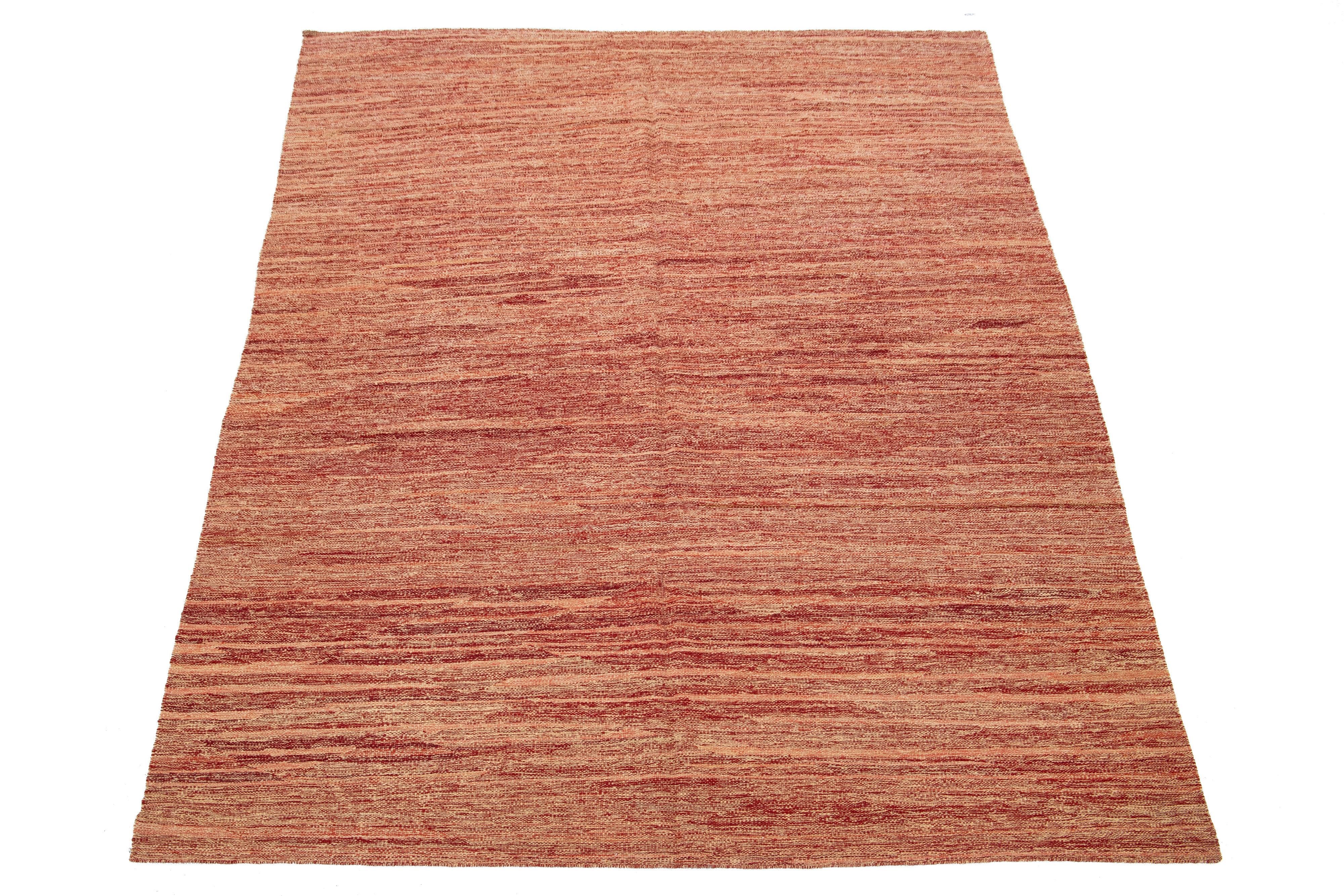 Questo tappeto presenta un moderno design Kilim a tessitura piatta in lana, con un motivo a strisce su una base color rosso-ruggine. 

Questo tappeto misura 7'4