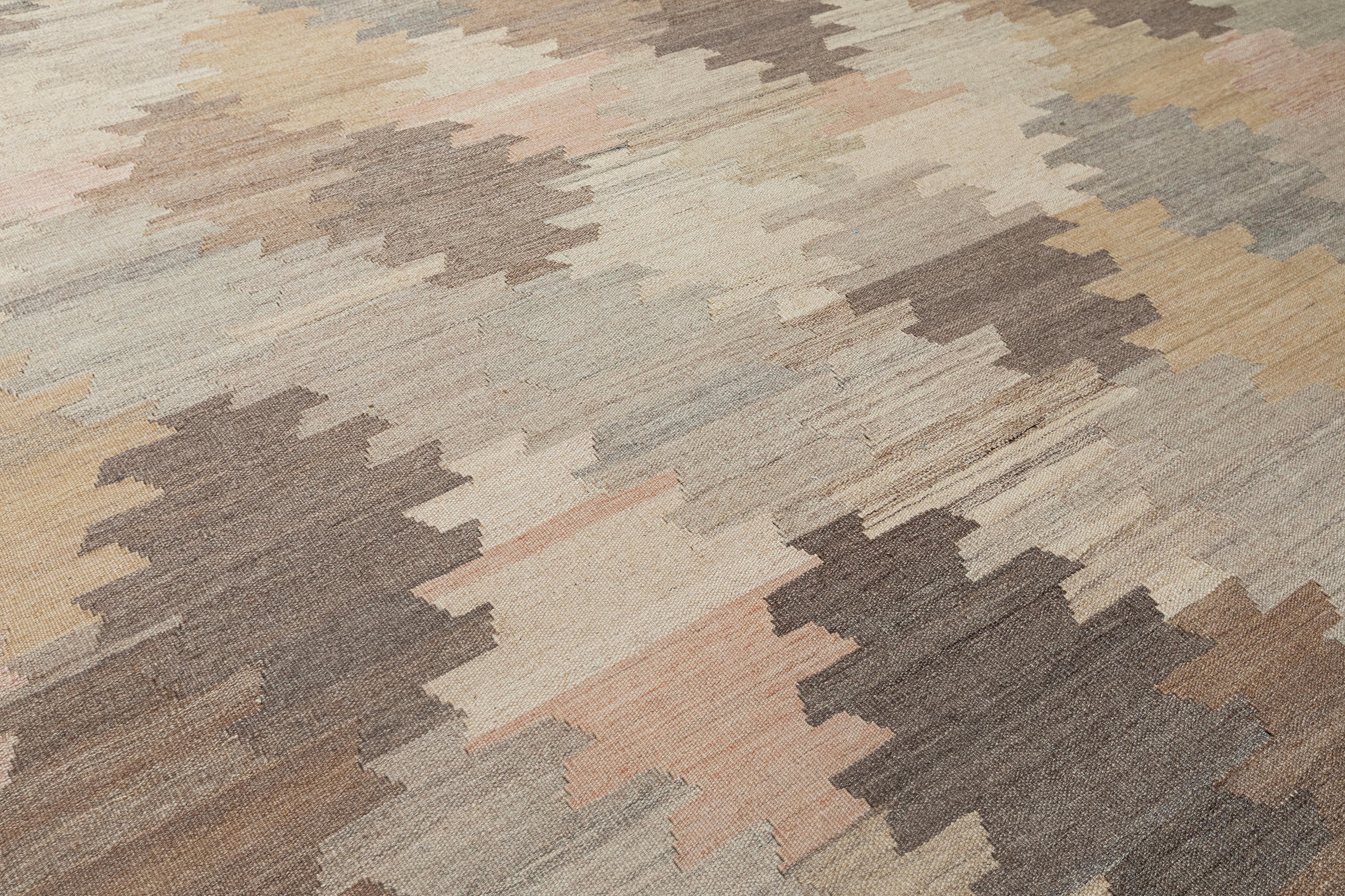 Dieser moderne flachgewebte Kelimteppich zeigt eine weiche und erdige Farbpalette mit ineinandergreifenden geometrischen Motiven in natürlichem Beige, Taupe, Sand und Blush. Der fachmännisch handgewebte Teppich aus 100 % Wolle verbindet