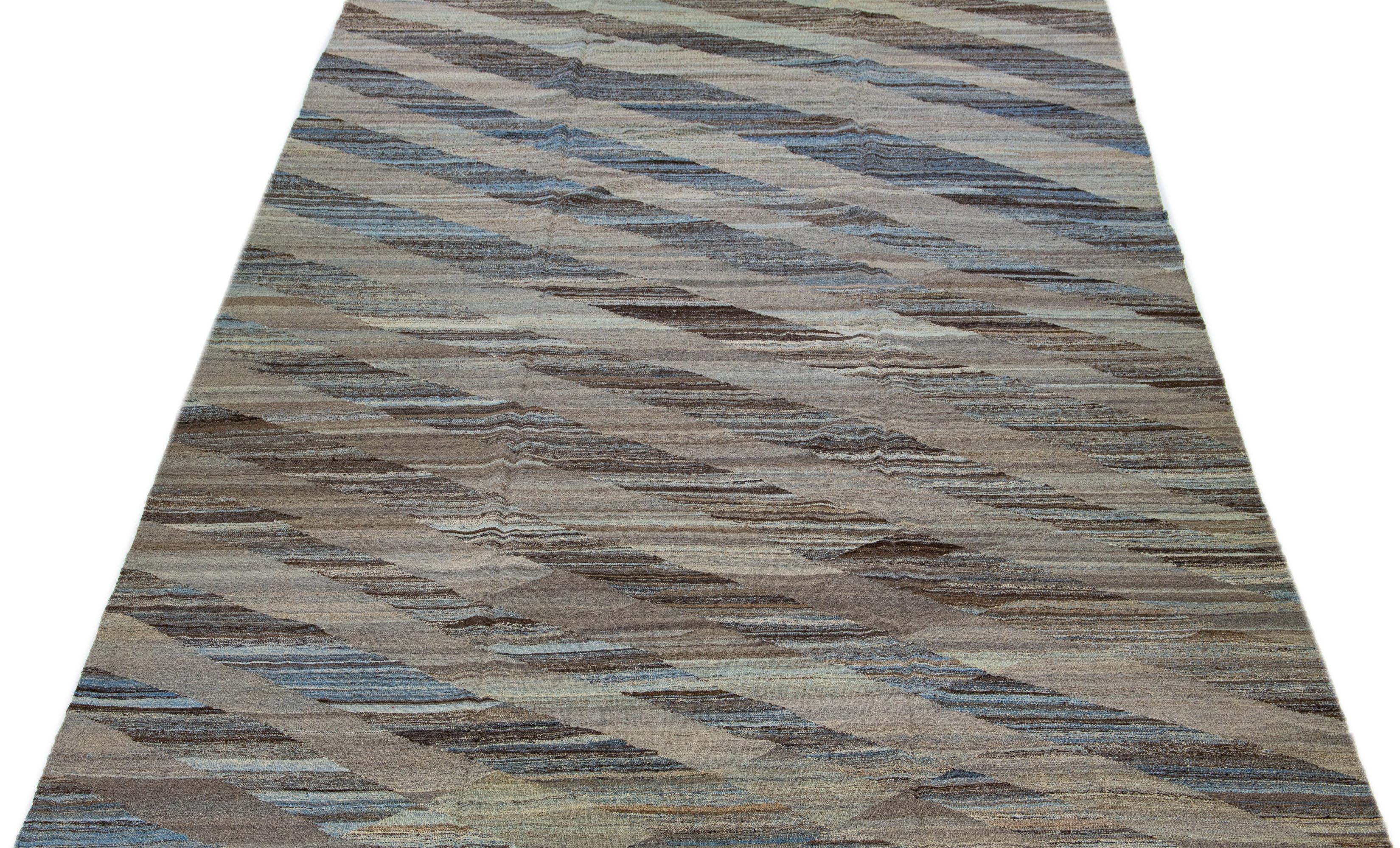 Der sorgfältig gefertigte Kilim-Teppich besticht durch sein modernes Design mit einem dominanten braunen Feld, das durch abstrakte geometrische Muster in Blautönen akzentuiert wird.

Dieser Teppich misst 10'8