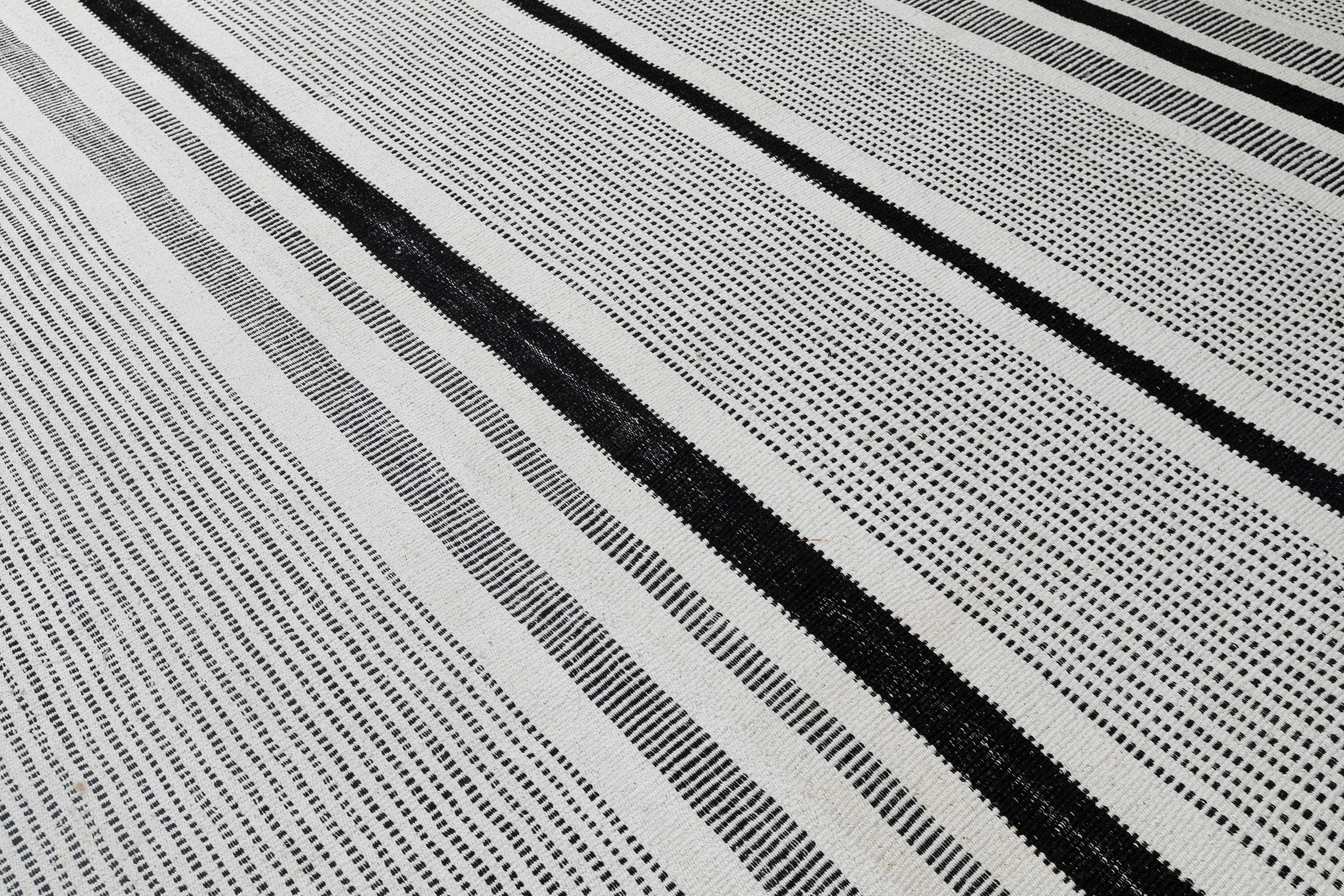 Questo tappeto moderno a tessitura piatta presenta un design a righe bianche e nere audace e minimalista, tessuto a mano con una ricca miscela di cotone naturale e lana nera. L'uso di fibre contrastanti conferisce profondità, consistenza e un ritmo
