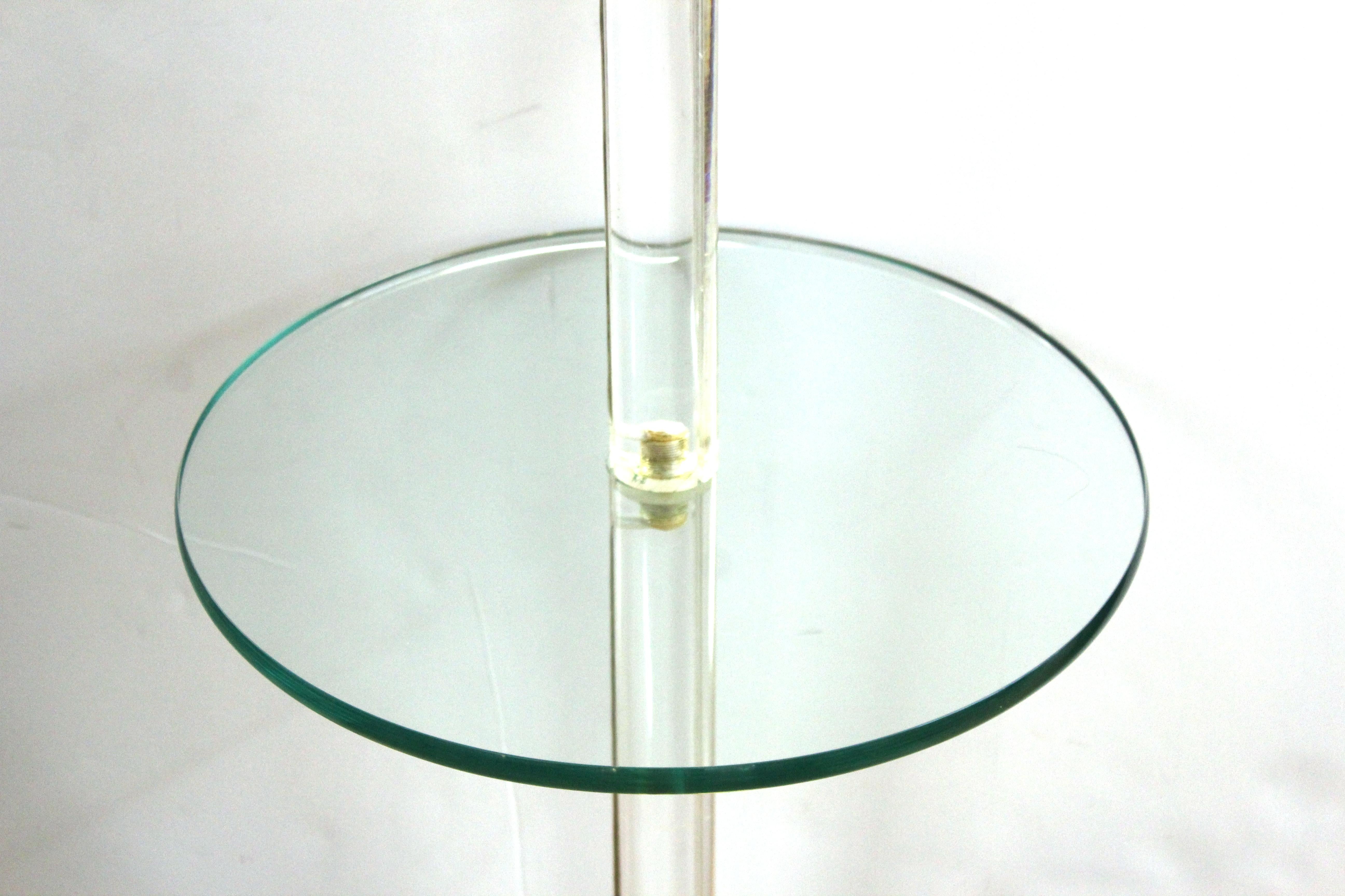 Modern floor lamp with Lucite stem and brass foot, with a circular glass surface mid-level acting as occasional or side table, attributed to Karl Springer. The Lucite has a slit for passing the cord, the upper part has a moving brass arm with two