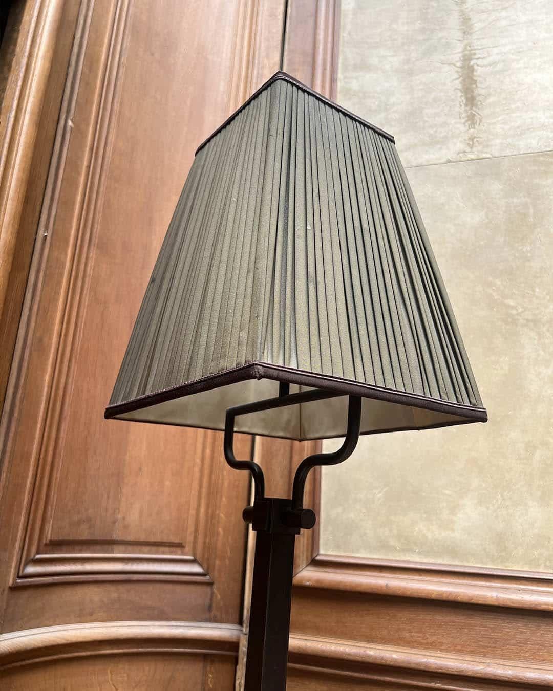 Elegant et discret, ce lampadaire est doté d'une élégante base métallique à section carrée au fini sombre subtilement patiné, complétée par un abat-jour en tissu plissé dans des tons sourds. Le design raffiné allie minimalisme moderne et élégance