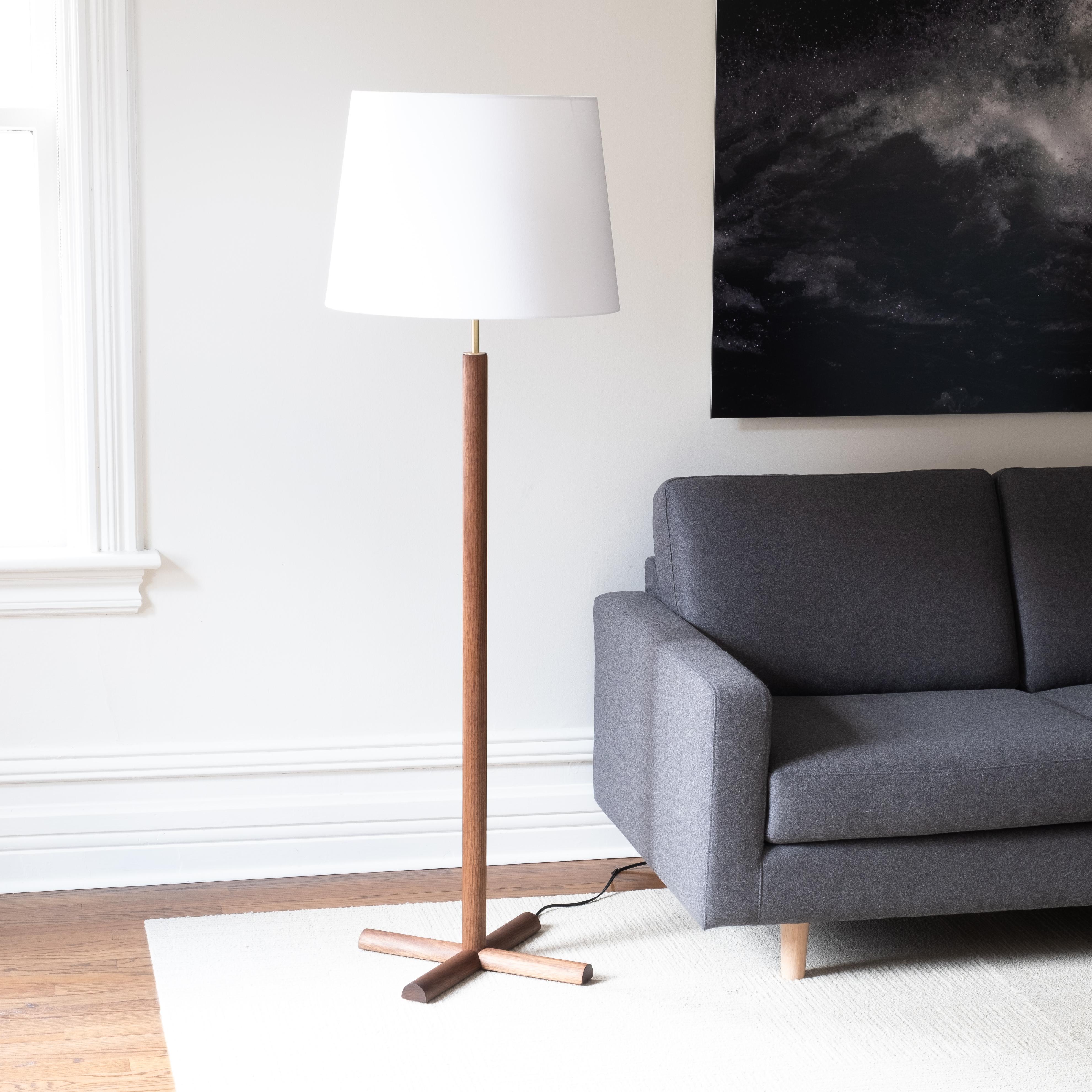 The Crux floor lamp combines minimalist forms, top-quality materials, and careful details.
The generous conical shade is supported by a clean column of turned wood, with an exposed section of brass hardware adding an elegant accent between the wood