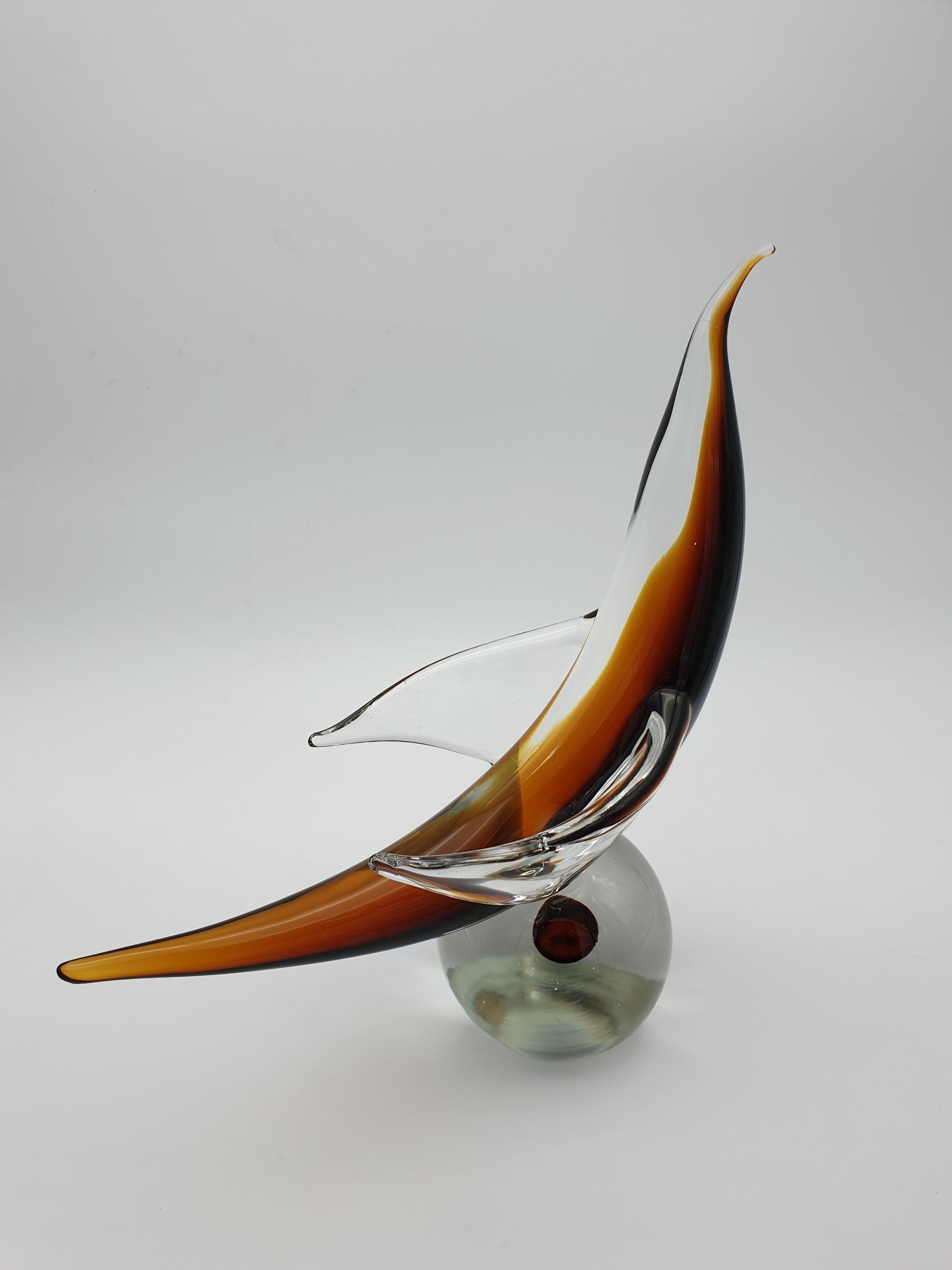 This unconventional/peculiar Murano glass sculpture was made by the glass factory Gino Cenedese e Figlio in the island of Murano and symbolizes a bird ready to take off. The tapered shape is made of clear glass with amber-colored touches, and it