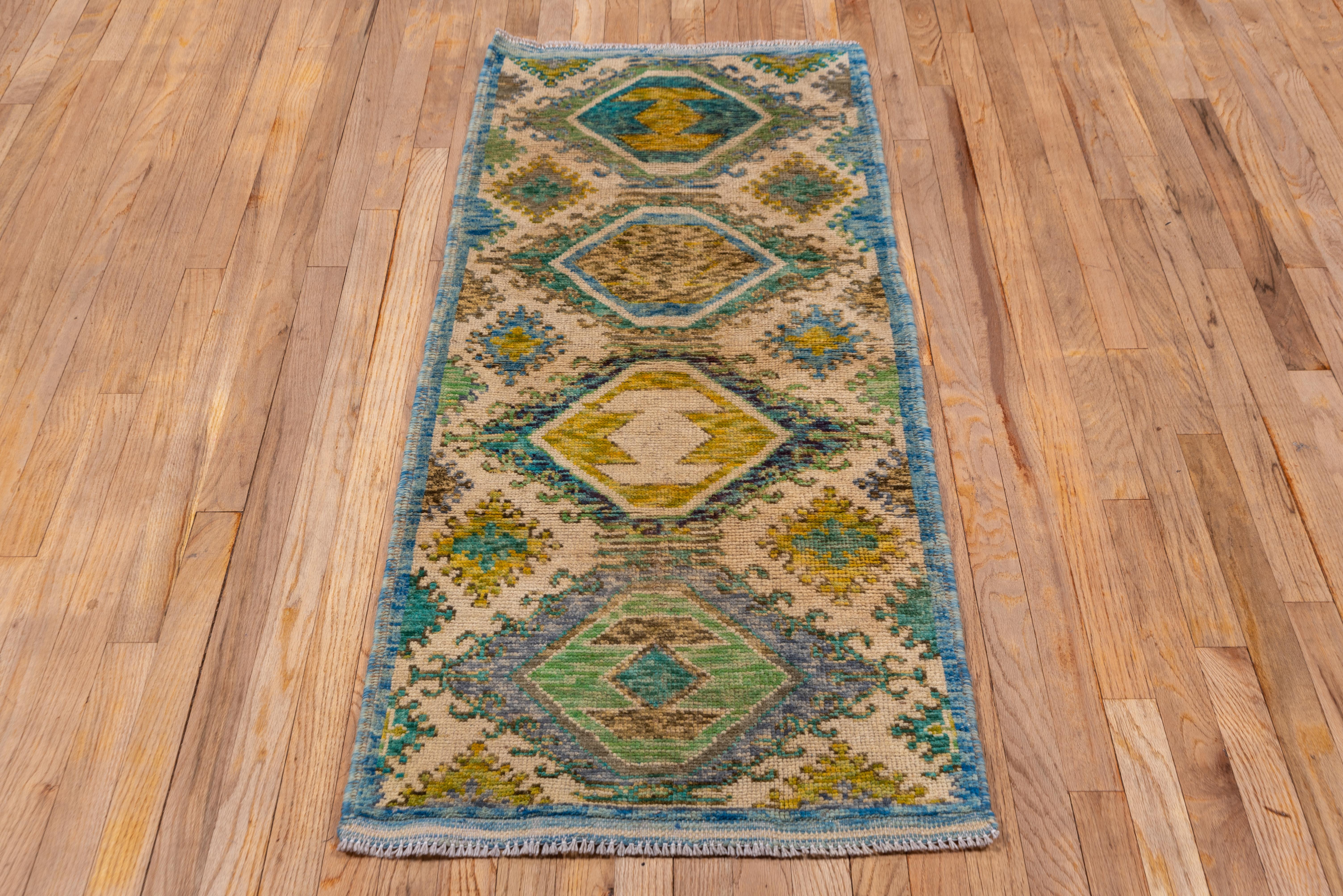 In a Kilim design with only the most minimal broken blue borders, the sandy straw field features four hooked hexagonal medallions in broken shades of light rust, light blue, dark blue, green and gold, with smaller hooked diamonds and side fillers