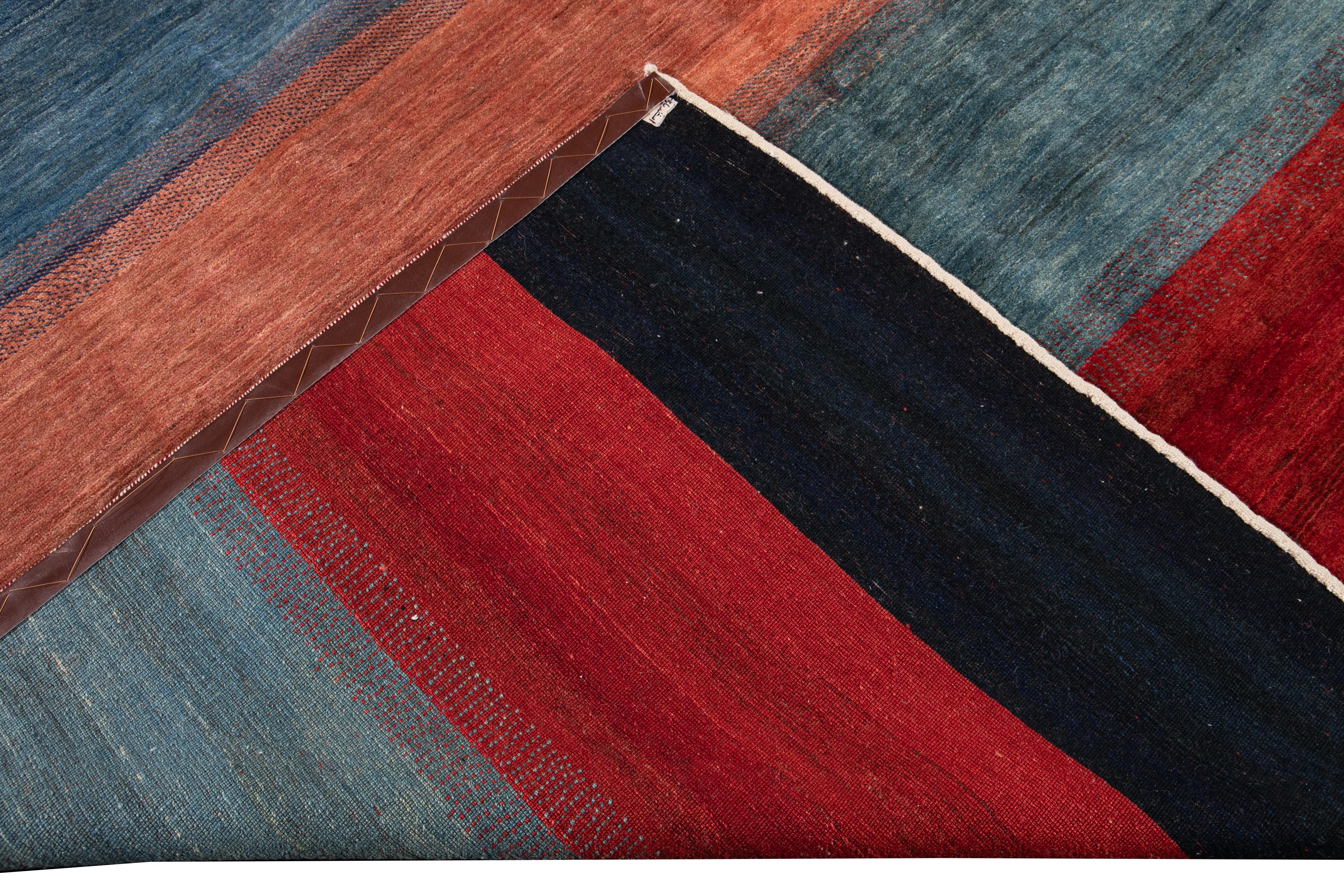 Beautiful contemporary Persian Gabbeh hand knotted wool rug. This Gabbeh rug has a gorgeous striped field with colors of red, blue, yellow, black, and gray all-over the design.

This rug measures: 8'6