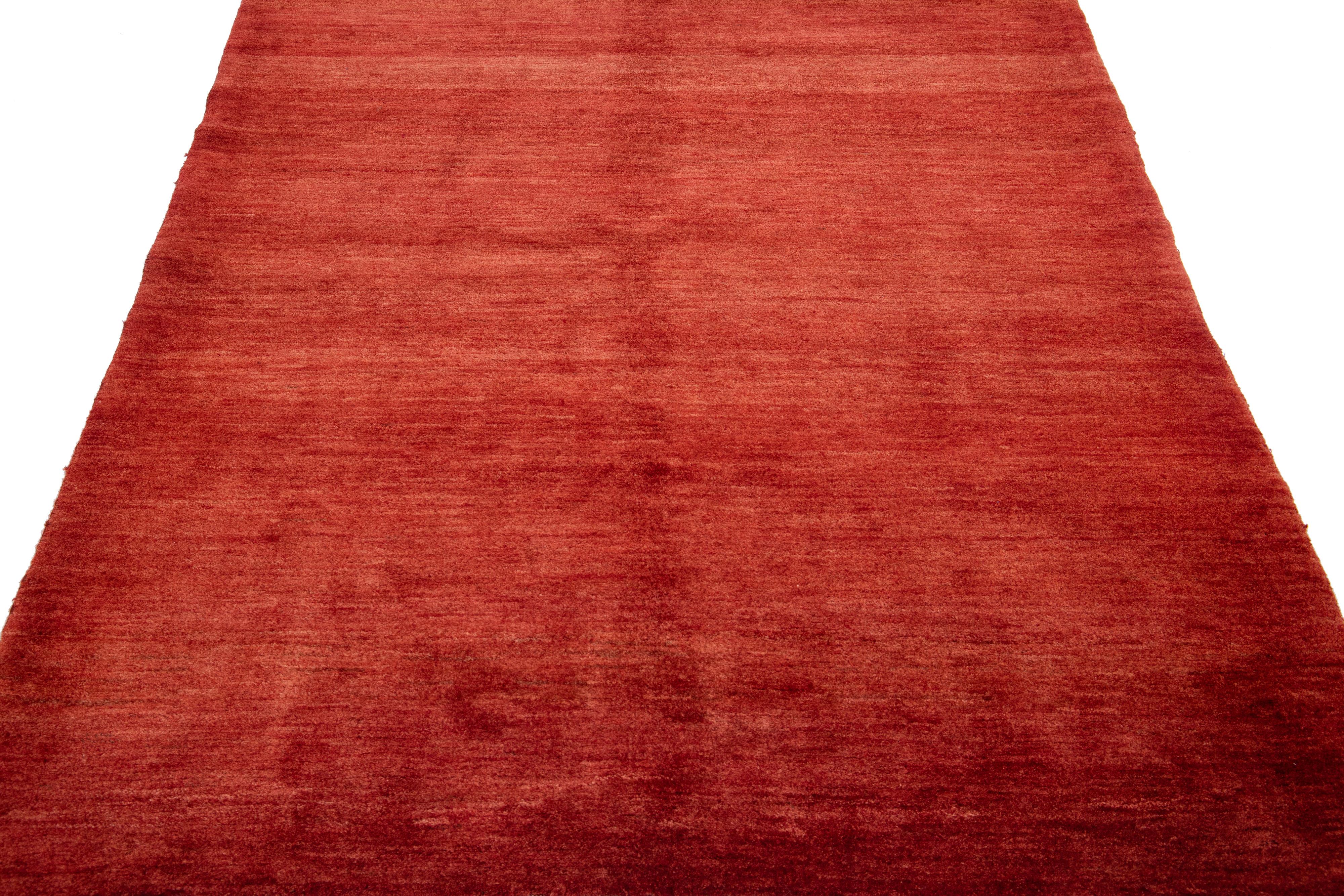 Magnifique tapis moderne en laine nouée à la main de style Gabbeh, avec un champ de couleur rouge-rouille. Cette pièce présente un magnifique motif solide sur toute sa surface.

Ce tapis mesure : 5'2