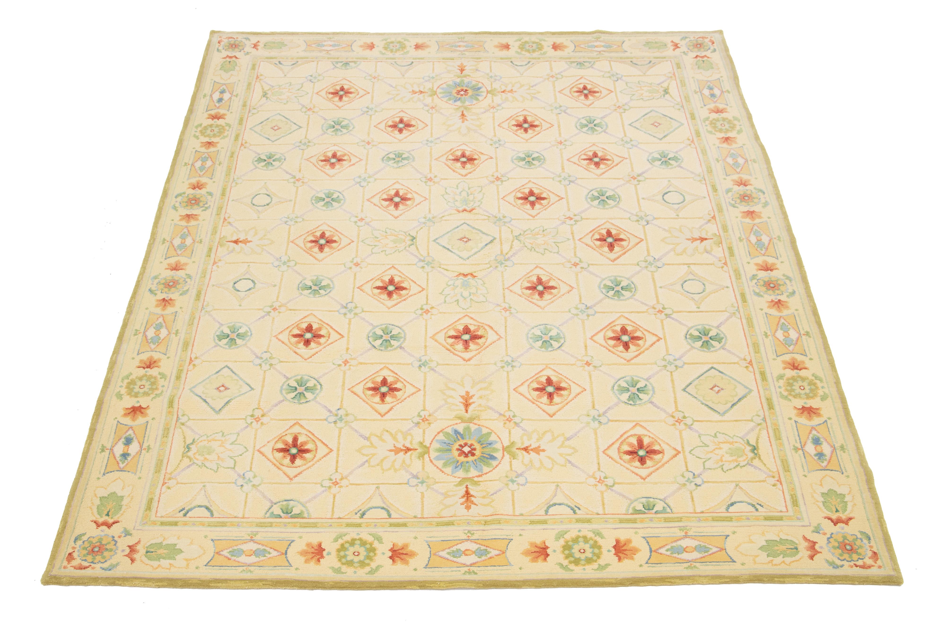 Un tappeto contemporaneo in lana indiana del XXI secolo con un campo di colore beige. Questo pezzo presenta dettagli intricati con splendidi colori verde, rosso e marrone, oltre a un meraviglioso motivo floreale. Sarebbe un'aggiunta perfetta alla