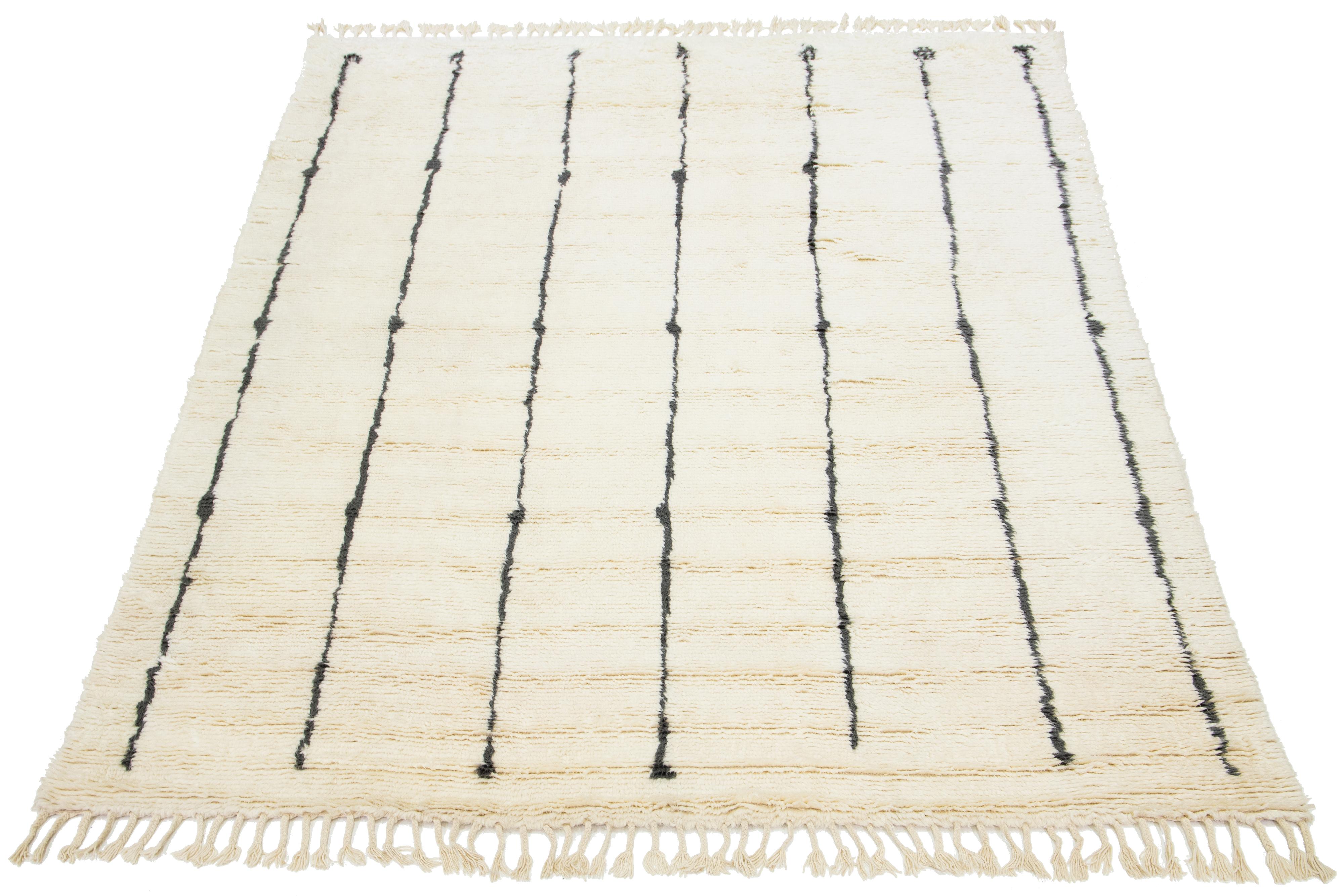 Questo bellissimo tappeto contemporaneo in lana annodato a mano in stile marocchino ha un campo e frange color avorio. Questo tappeto in peluche presenta un meraviglioso disegno lineare nero.

Questo tappeto misura 9' x 11'11