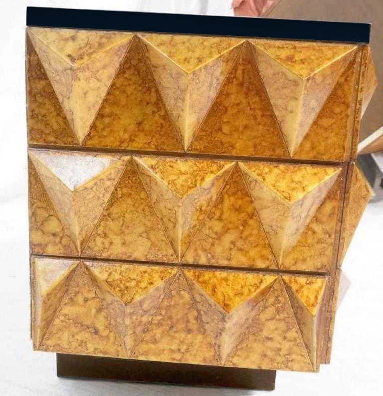 Cassettiera moderna borchiata laccata dorata, con piano laccato nero dotato di due cassetti, uno più piccolo e il cassetto inferiore di dimensioni doppie, sollevato su una base a piedistallo laccata.

