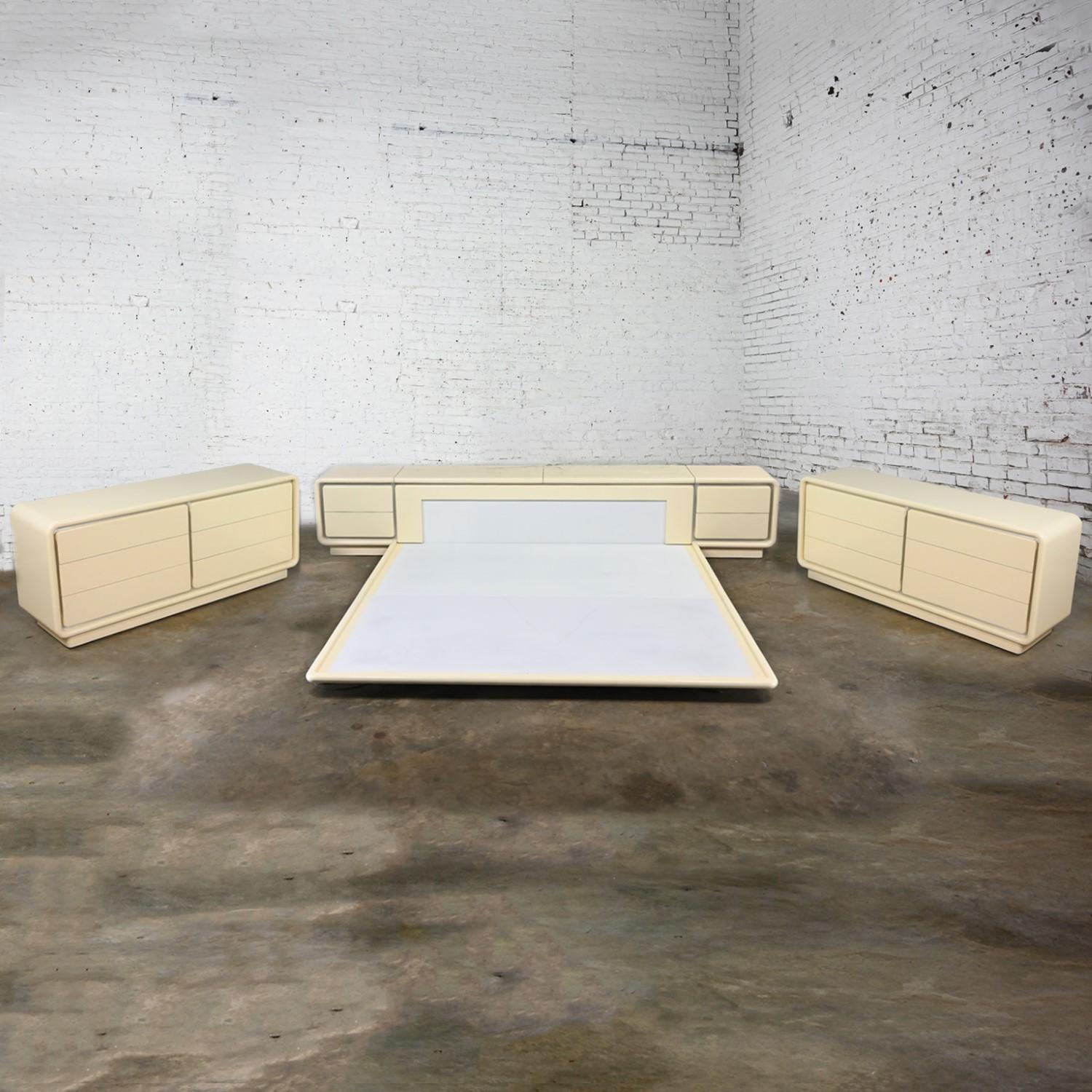Incredible vintage Modern to Postmodern Glenn of California bedroom set including king-sized headboard, platform, pair of nightstands, and pair of dressers or credenzas with off white lacquer finish, aluminum strip accents, and lighting underneath