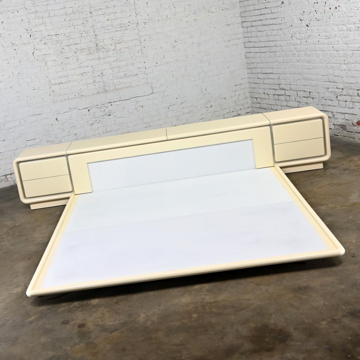 Magnificent vintage Modern to Postmodern king-sized bed including headboard, platform, and pair of nightstands by Glenn of California with off white lacquer finish, aluminum strip accents, and original lighting underneath the platform. Beautiful