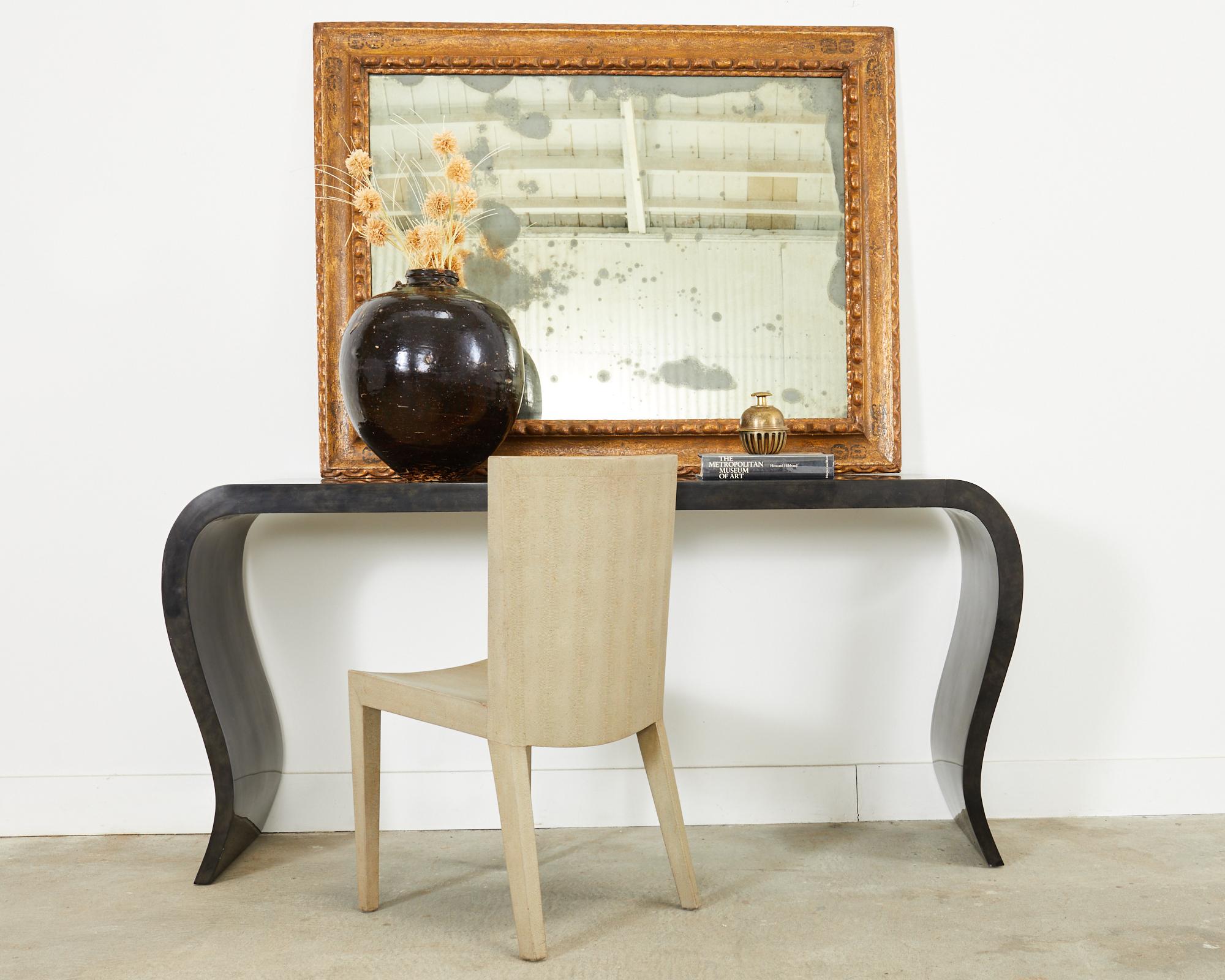 Dramatic goatskin parchment veneered console table crafted by Scala Luxury in the modern style. The table has gracefully curved legs in an hourglass shape with a dark rich parchment or vellum leather veneer. Nearly 6 foot long with heavy, solid