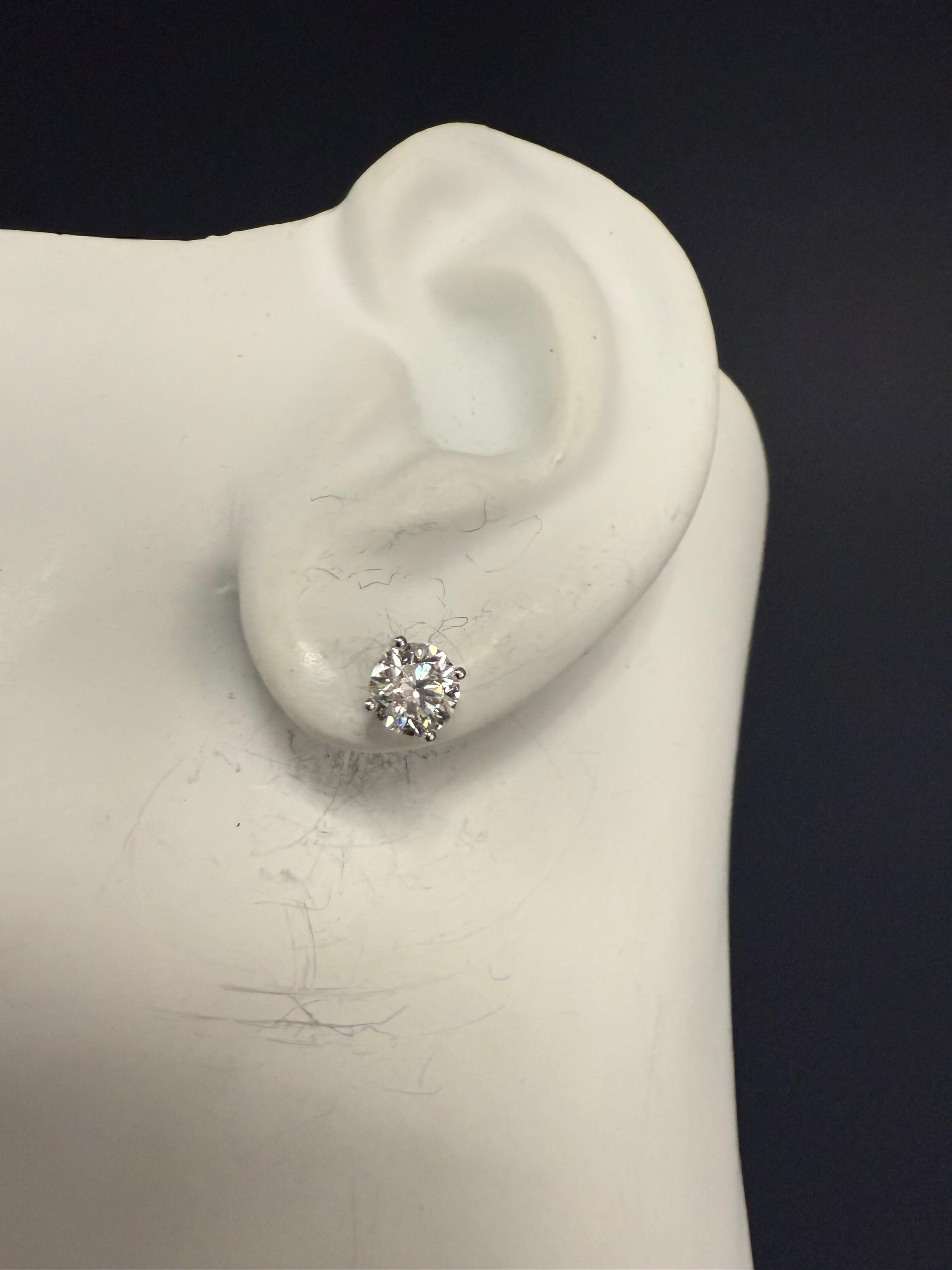 Modern 14K white gold martini-style stud earrings set with 1.43 carats of natural round brilliant colorless diamonds. 
The first stone is a 0.70 carat ideal cut, laser-inscribed diamond graded by EGL USA, with E color and SI1 clarity, measuring