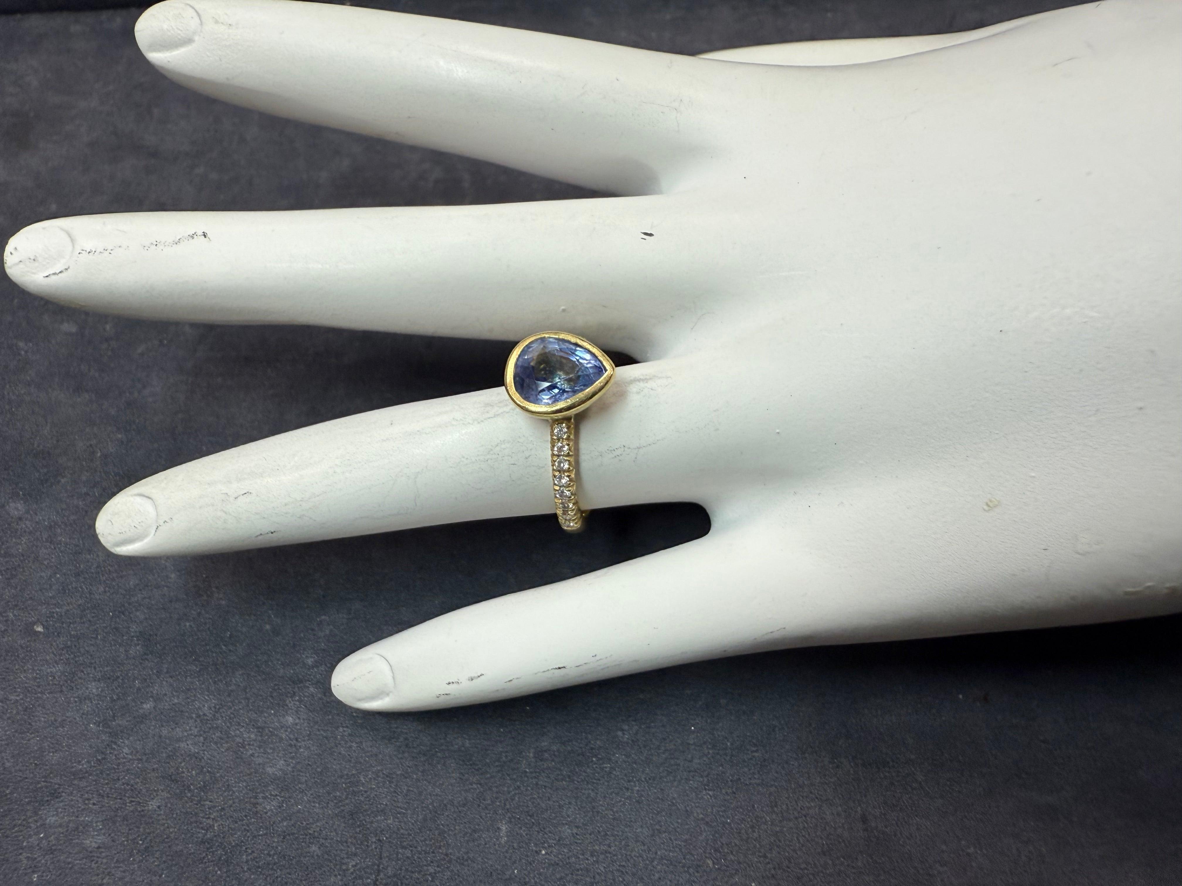 Modern 18K yellow gold ring with a brushed finish, featuring a bezel-set natural light blue pear-shaped sapphire measuring approximately 8.25 x 7.1 x 4.6 mm and weighing an estimated 2.00 carats. 
Accented by 16 natural round brilliant colorless