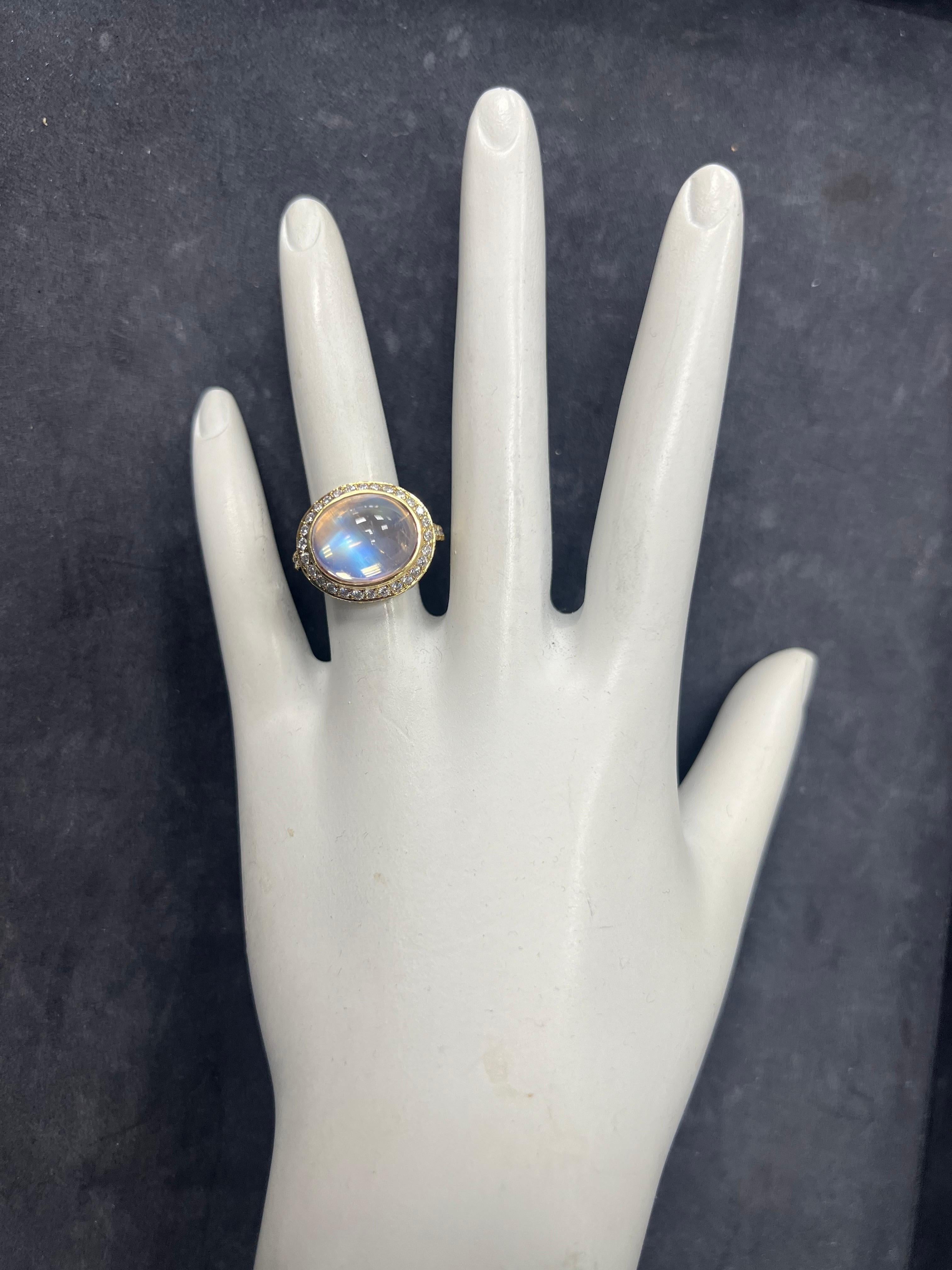 Ein seltener 6 Karat (ca.) blauer Mondstein-Feldspat, horizontal in einem Cocktailring gefasst. Der mittlere Mondstein misst 13x10,7x7 mm. Eingeschlossen sind etwa 1,25 Karat von siebenundsiebzig natürlichen, runden, farblosen Diamanten. Die Größe