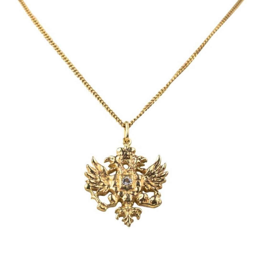 The Romanov double-headed eagle with outspread wings, its claws clutching orb and sceptre, surmounted by an imperial crown and centered by a bright antique-cut diamond, the reverse in smooth polished gold. Chain not included.

1 1/8 in. (2.9 cm.)