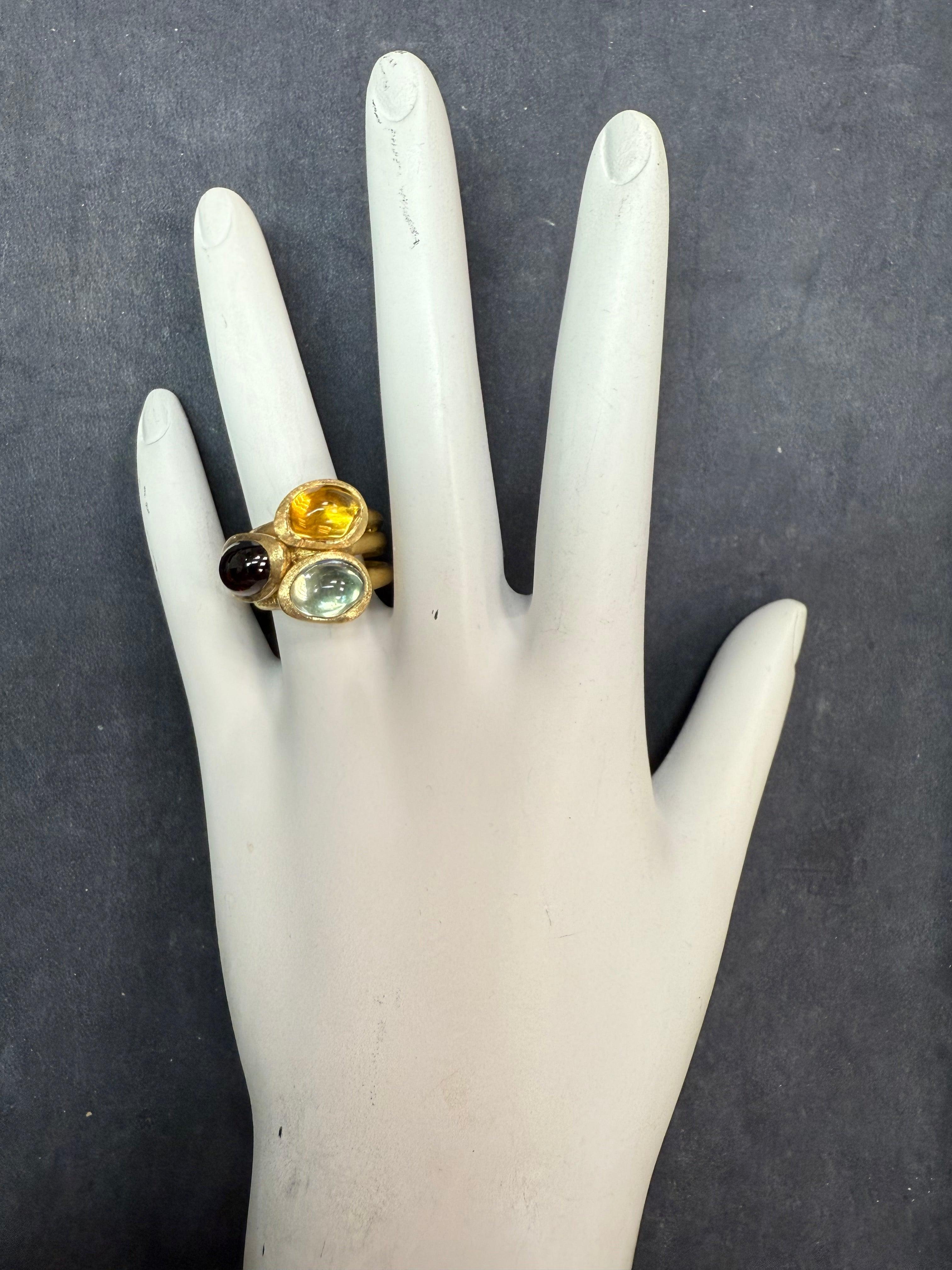 Bague d'apparat du designer italien Marco BICEGO, estampillée 750 pour l'or jaune 18 carats. Trois cabochons multicolores, dont un quartz, mesurant chacun environ 8,5 x 6,5 mm. L'anneau a une largeur de 17 mm en haut et se rétrécit à 8 mm en bas. Il