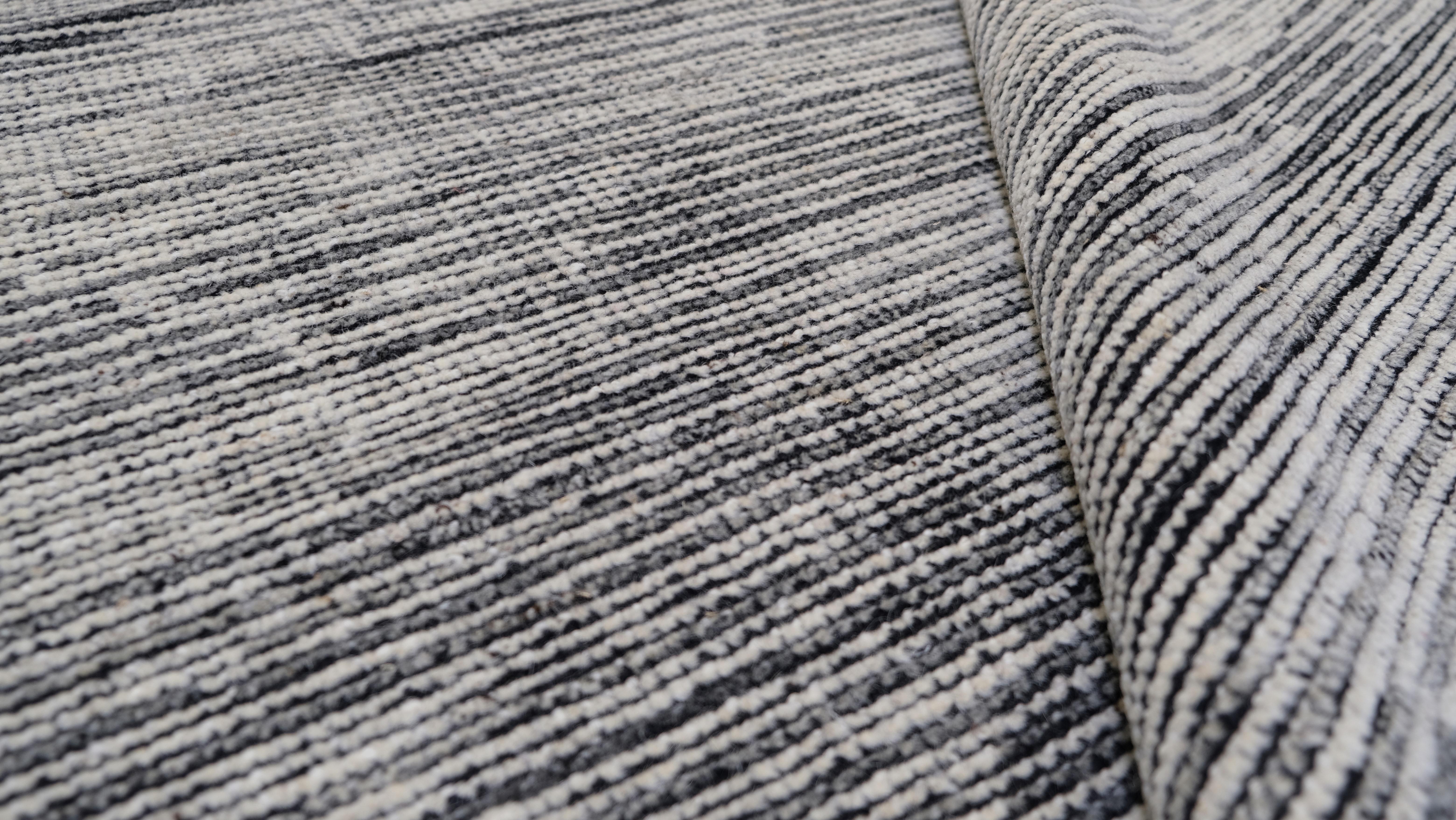 Esta alfombra de lana anudada a mano presenta un elegante y sutil dibujo hexagonal mezclado a la perfección con finas texturas lineales, creando una sofisticada estética monocromática. Los suaves tonos grises y marfil claro ofrecen un atractivo