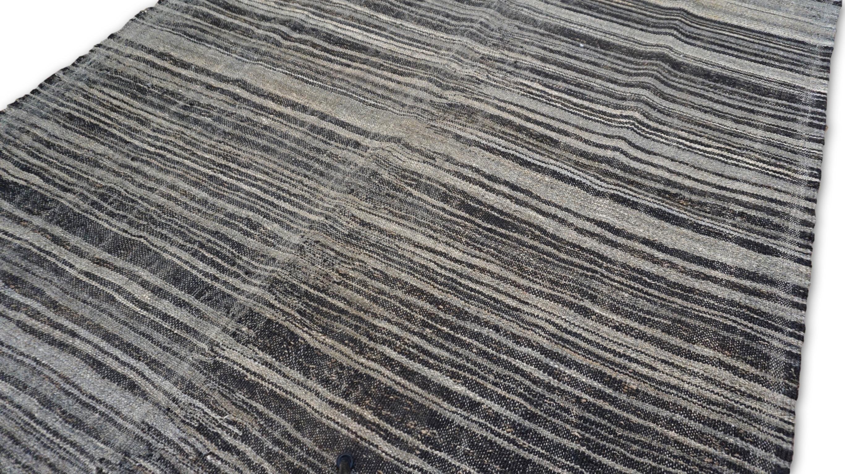 Questo tappeto in lana intrecciata a mano è un esempio lampante di minimalismo moderno fuso con l'artigianato tradizionale. Caratterizzato da un motivo organico a strisce orizzontali di larghezza variabile, il design crea una texture visiva