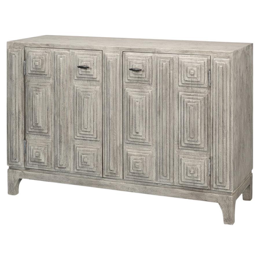Crafted from solid wood, this statement piece features a meticulously hand-carved geometric pattern adorning its double doors, creating a bold, three-dimensional effect. The soft, rustic gray finish enhances the textured surface, lending a weathered