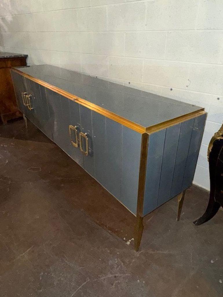 The Modern Gray Murano Glass and Brass Sideboard is a stylish piece of furniture for the home. This sideboard features glass doors and brass details, adding a touch of elegance to any room. The sleek gray color adds a modern and contemporary twist