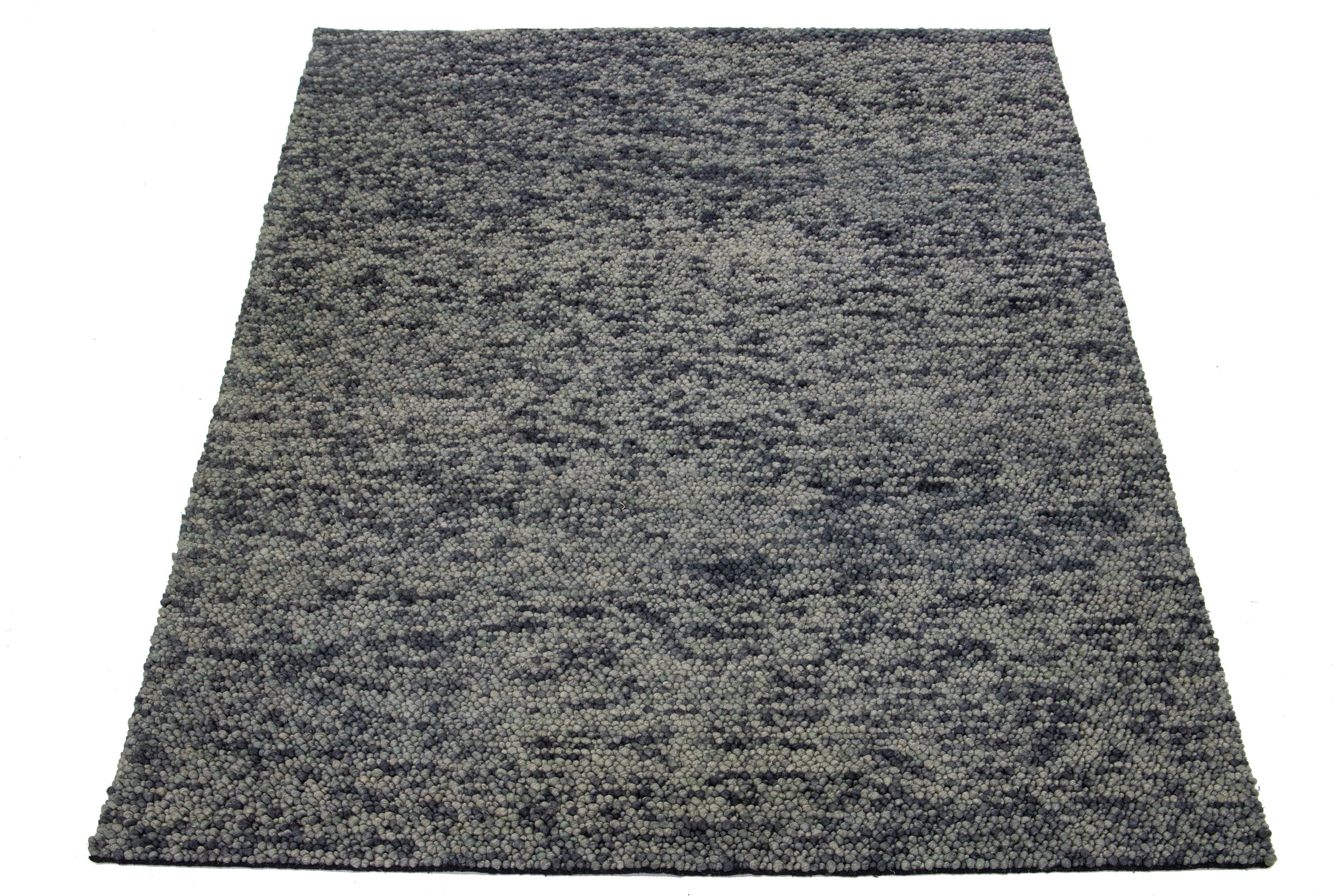 Dieser schöne, modern strukturierte, handgeknüpfte Wollteppich aus unserer Sasco Collection zeichnet sich durch ein Farbfeld aus Grau und Blau aus. Der Teppich besticht außerdem durch ein abstraktes, strukturiertes Muster, das an Kieselsteine