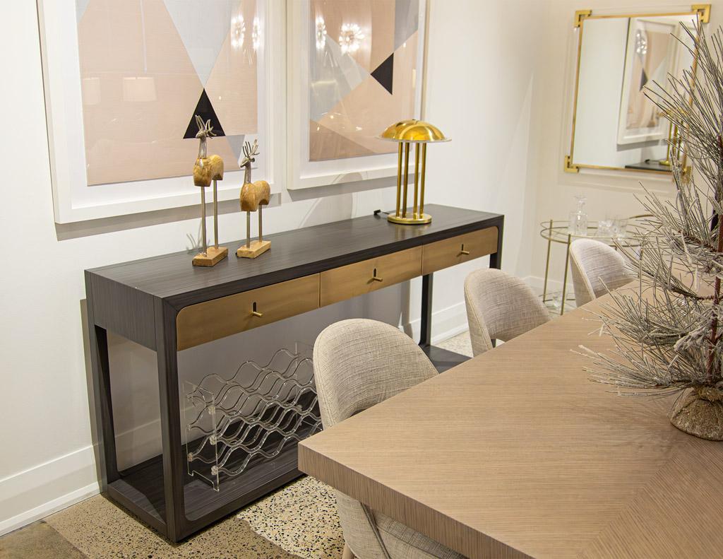 La console Fulton de Joseph Jeup est le complément idéal de tout espace moderne. Cette table console élégante et raffinée présente des façades de tiroirs et des ferrures en laiton, des bois de noyer et une finition laquée grise satinée remarquable.