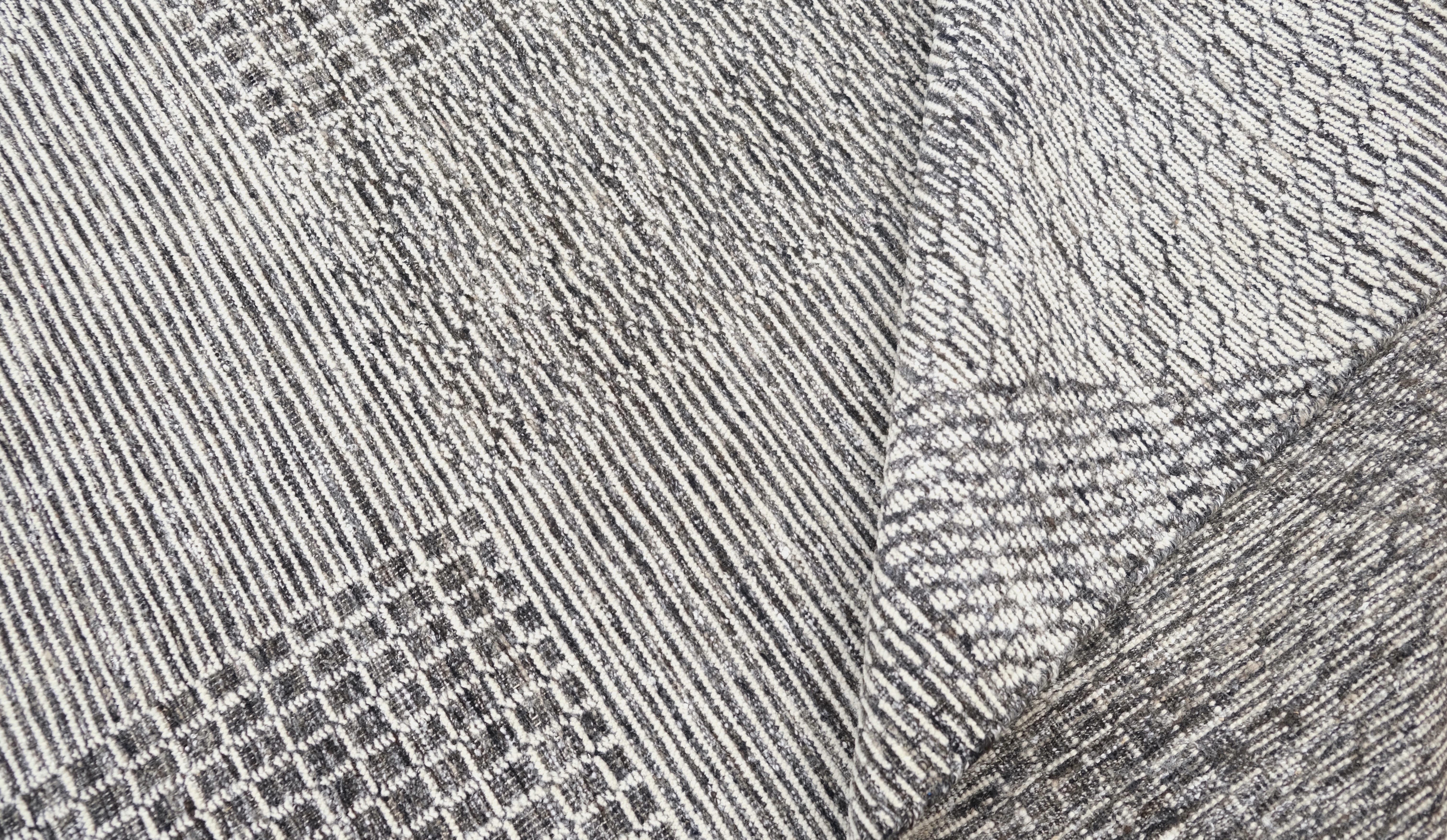Mejora tus interiores con esta alfombra contemporánea de lana anudada a mano. Con un sofisticado diseño geométrico cuadriculado, esta alfombra combina varios motivos y texturas intrincados en una paleta gris monocromática. La interacción de
