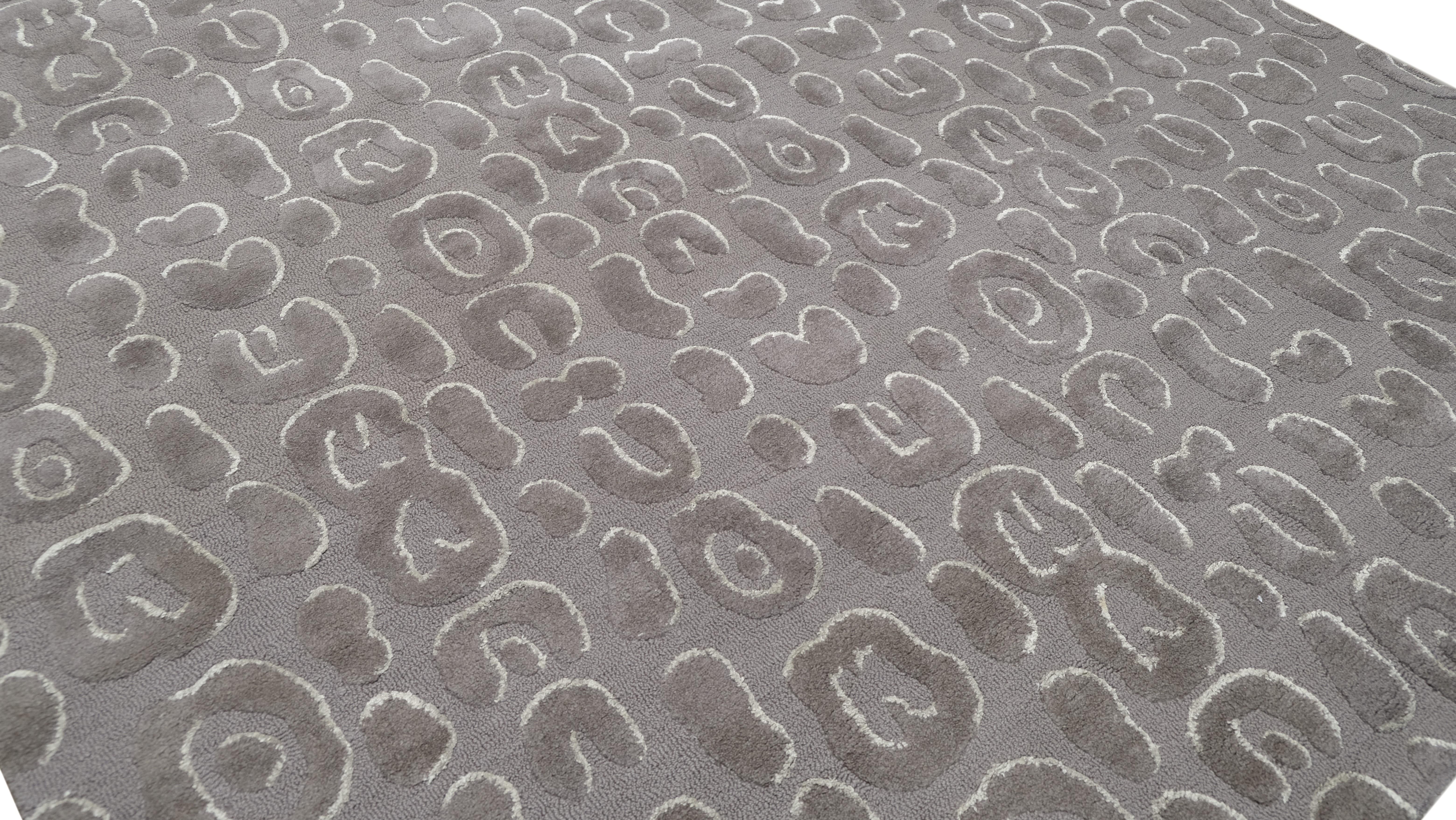 Ce tapis en laine tufté à la main est un mélange étonnant de luxe moderne et d'art complexe. Doté d'un motif abstrait en relief de formes organiques sur un fond gris riche et monochrome, ce tapis crée un effet dimensionnel captivant, ce qui en fait