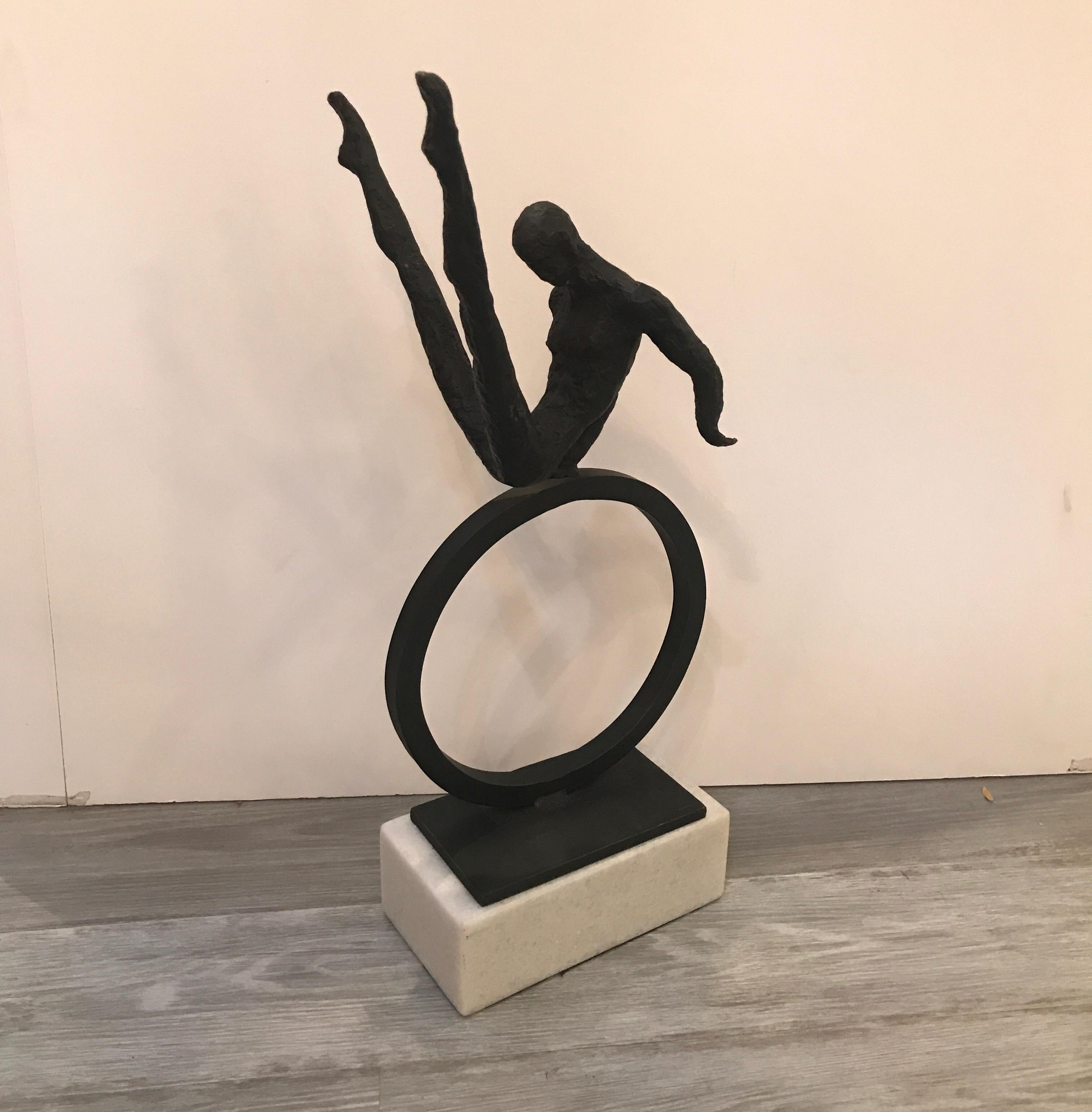 A cast iron and marble sculpture of a gymnast. The textured surface with a patinated finish with a white rectangular marble base.