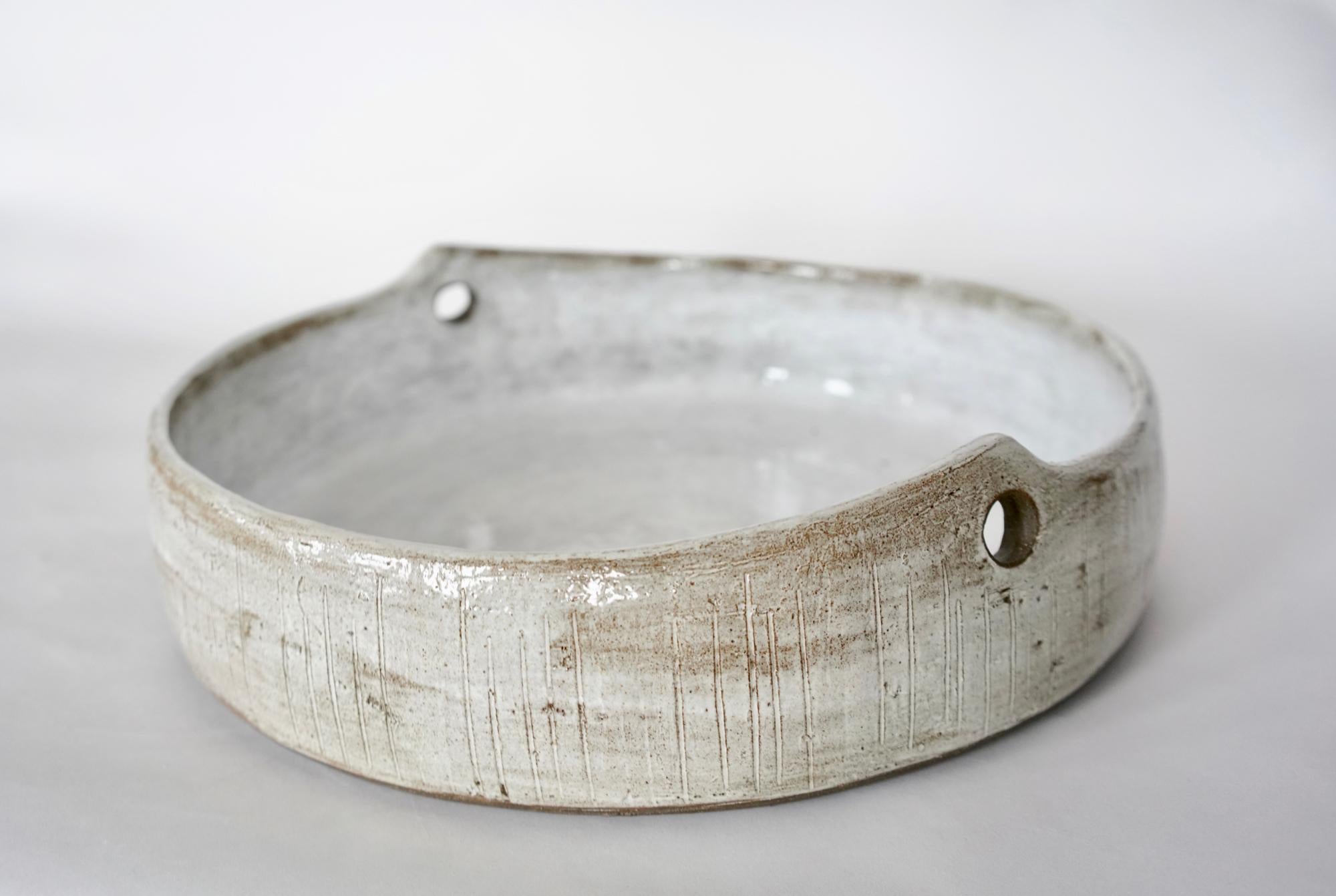 Large, wide and low ceramic stoneware serving bowl or center piece.
This Modern yet rustic piece features subtle hand carved markings on the exterior. A mottled glossy white glaze over dark clay reveals the clay body and adds depth of color, giving