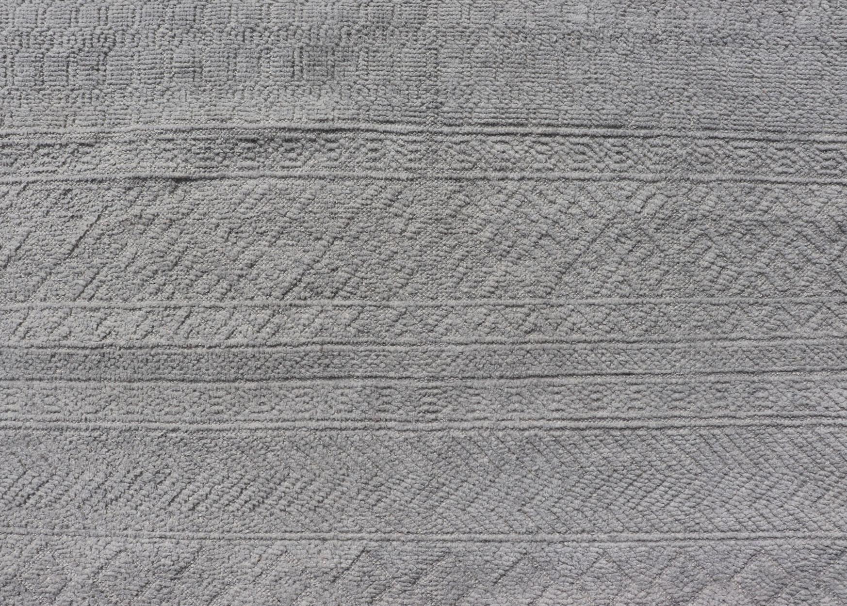 Questo moderno tappeto tribale Oushak è stato annodato a mano in lana. Il tappeto presenta un moderno disegno sub-geometrico all-over in color crema e un bordo complementare a più livelli che abbraccia l'intero pezzo; questo tappeto si adatta