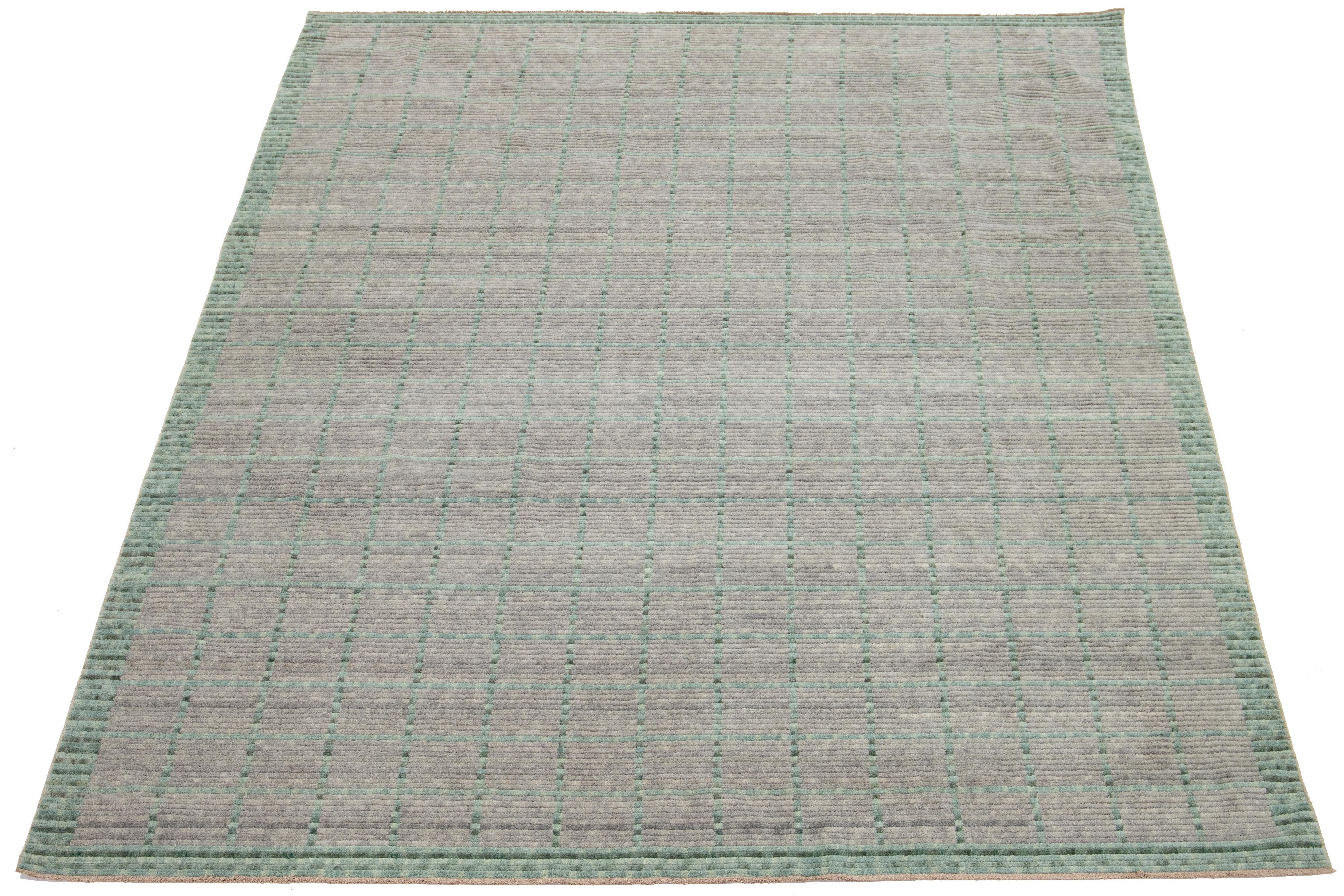 Dieser handgewebte moderne Wollteppich ist ein echter Hingucker. Der elegante hellgraue Hintergrund ist die perfekte Leinwand für das verschlungene geometrische Muster in leuchtendem Grün, das jeden Raum optisch aufwertet. 

Dieser Teppich misst
