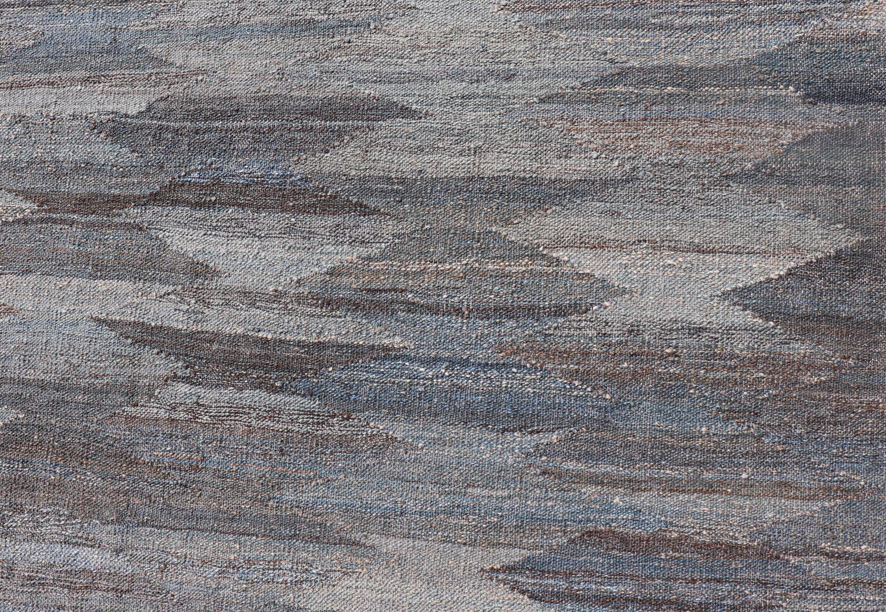 Dieser flachgewebte Stammeskelim wurde von Hand gewebt. Der Teppich zeichnet sich durch ein modernes unifarbenes/diamantenes Design aus, das in grauen, blauen und erdigen Tönen gehalten ist. Damit passt dieser Teppich hervorragend zu einer Vielzahl
